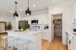 Modern kitchen featuring a large island with a light-toned countertop, white cabinetry with black hardware, stainless steel appliances, and wood-finish flooring
