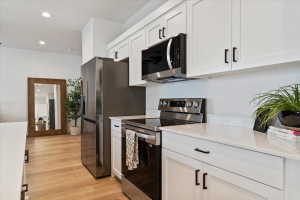 Modern kitchen featuring stainless steel appliances, white cabinetry, integrated microwave, and light wood-finish flooring