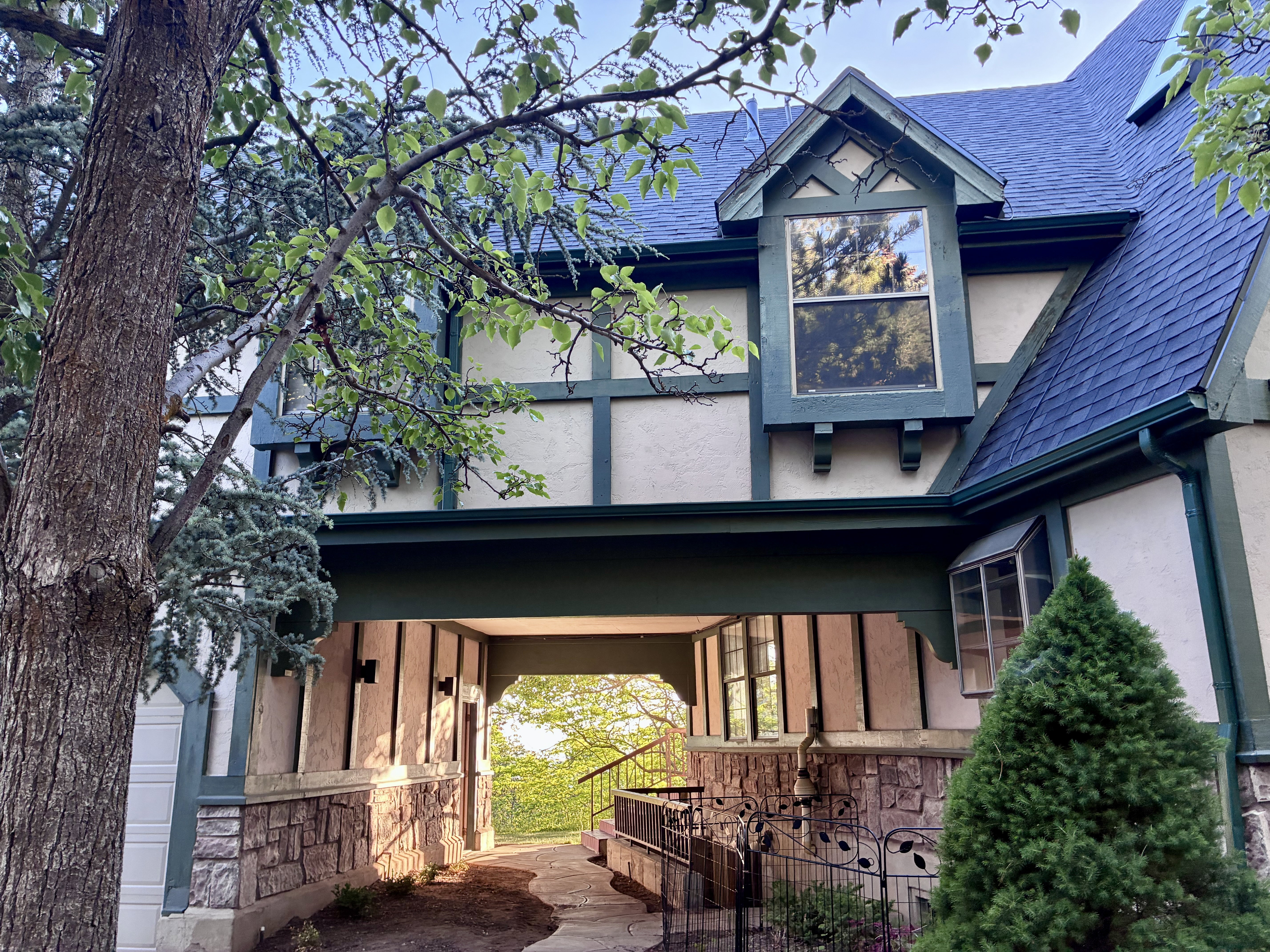 Tudor-style exterior showcasing a prominent dormer window, dark blue shingle roof, stone foundation accents, and a distinctive covered entryway