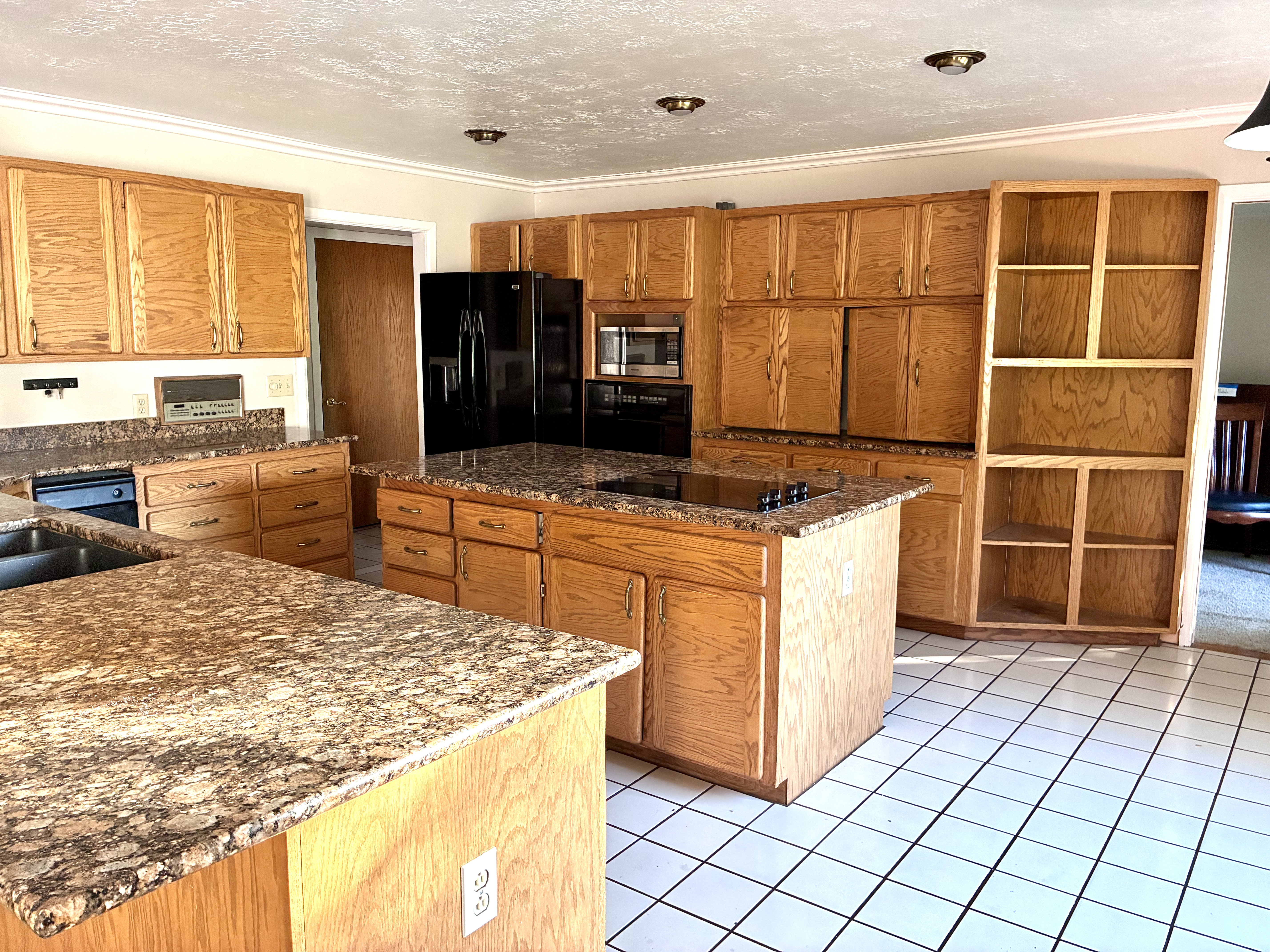 Kitchen featuring extensive wood cabinetry, granite-finish countertops, a central island with an integrated cooktop, and white square floor tiling