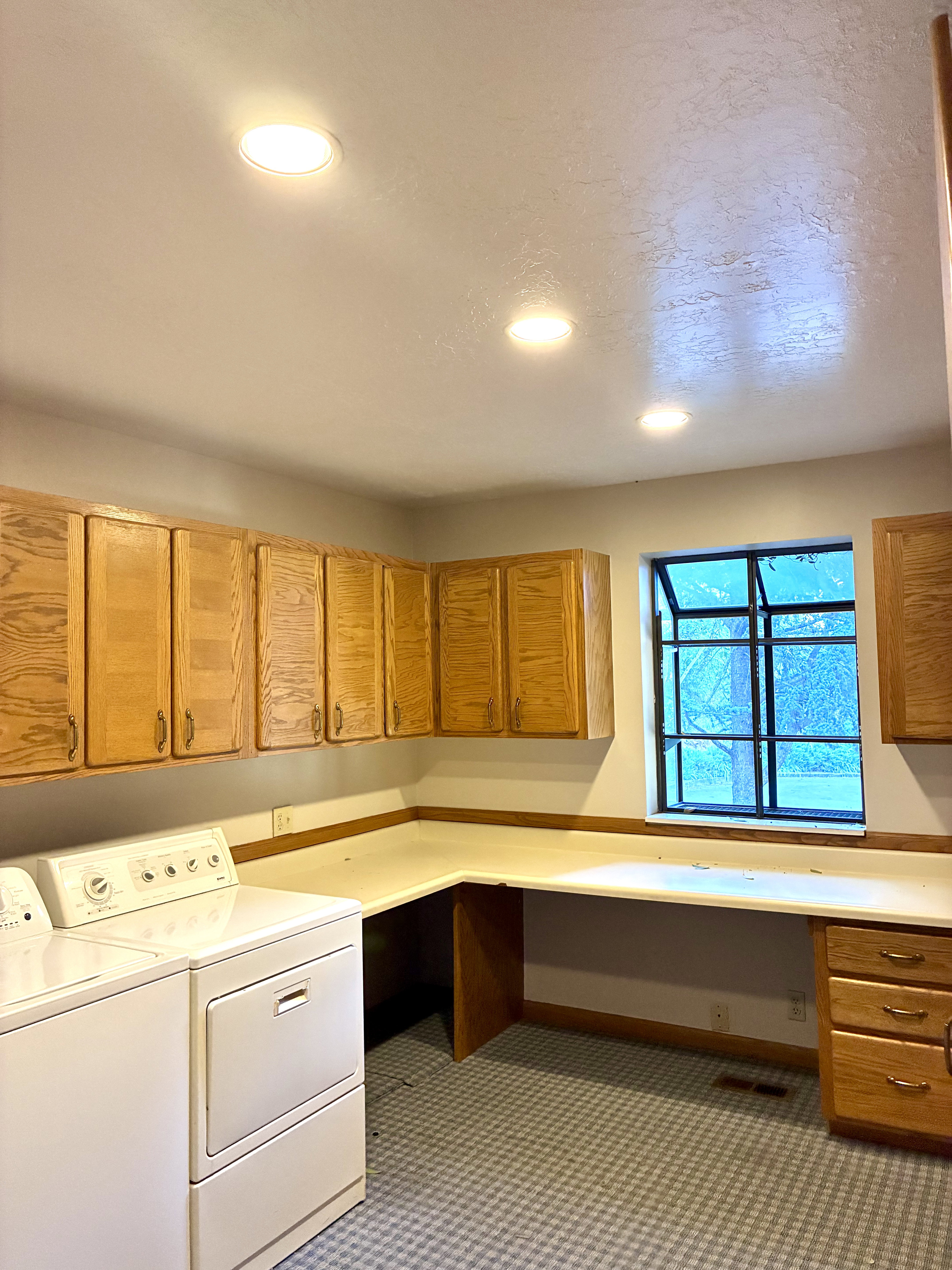 Functional utility room featuring extensive built-in cabinetry, an integrated L-shaped countertop, a window with exterior views, patterned flooring, and recessed ceiling lighting