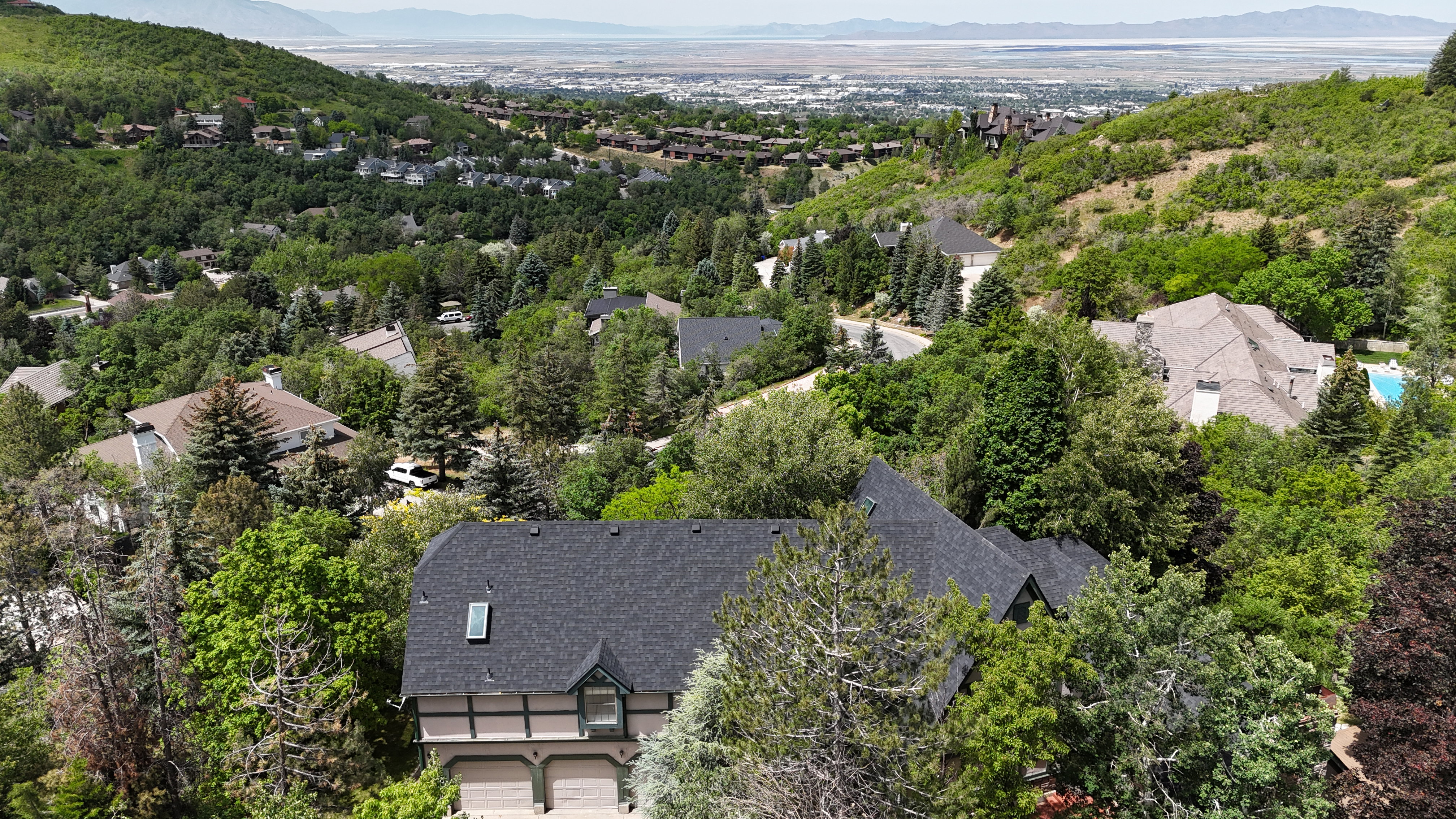 Hillside property surrounded by mature trees, featuring a dark shingle roof with an integrated skylight