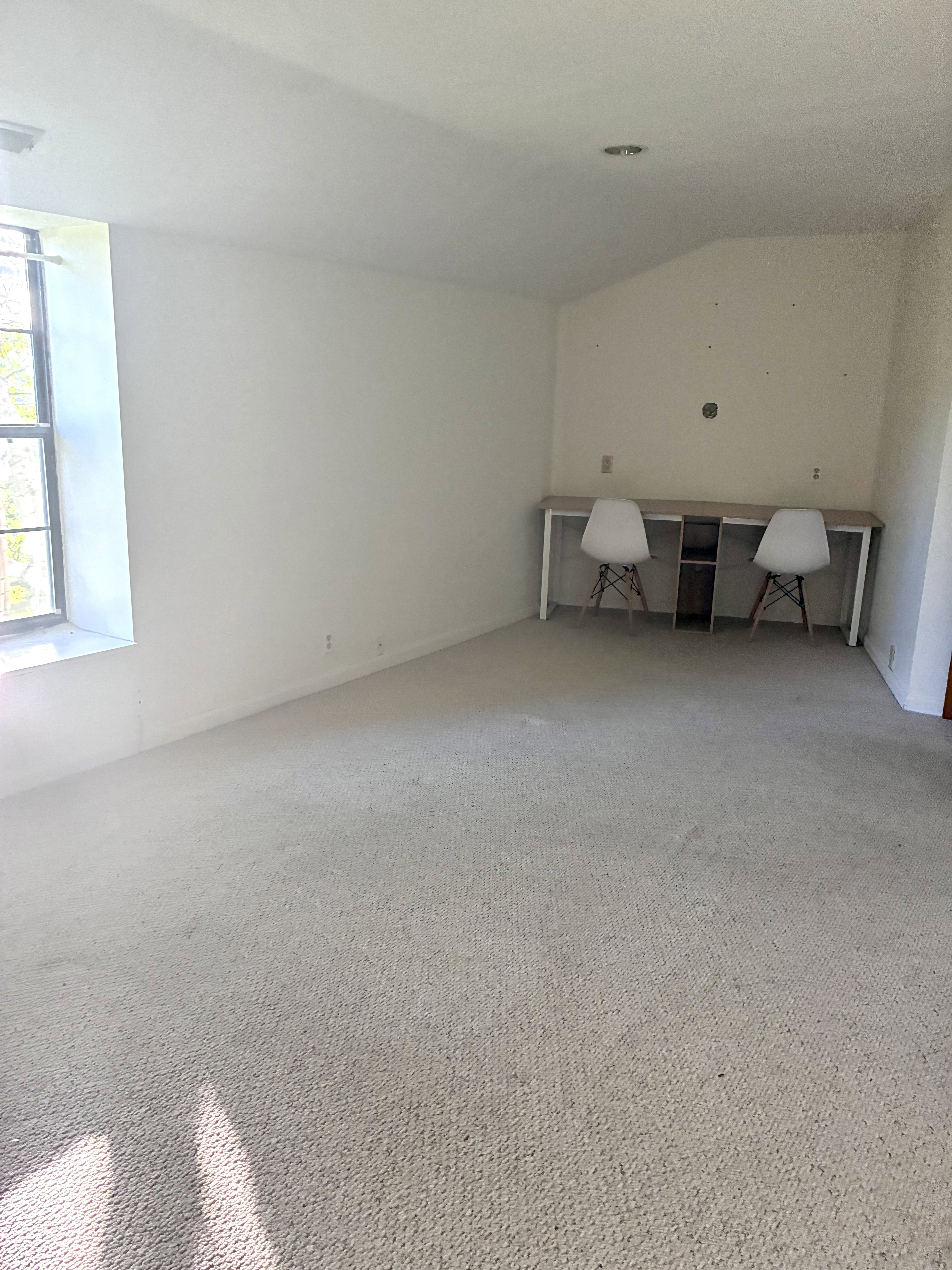 Carpeted room featuring a built-in wood-finish desk with white legs and a central storage unit, a sloped ceiling portion, and a recessed ceiling light