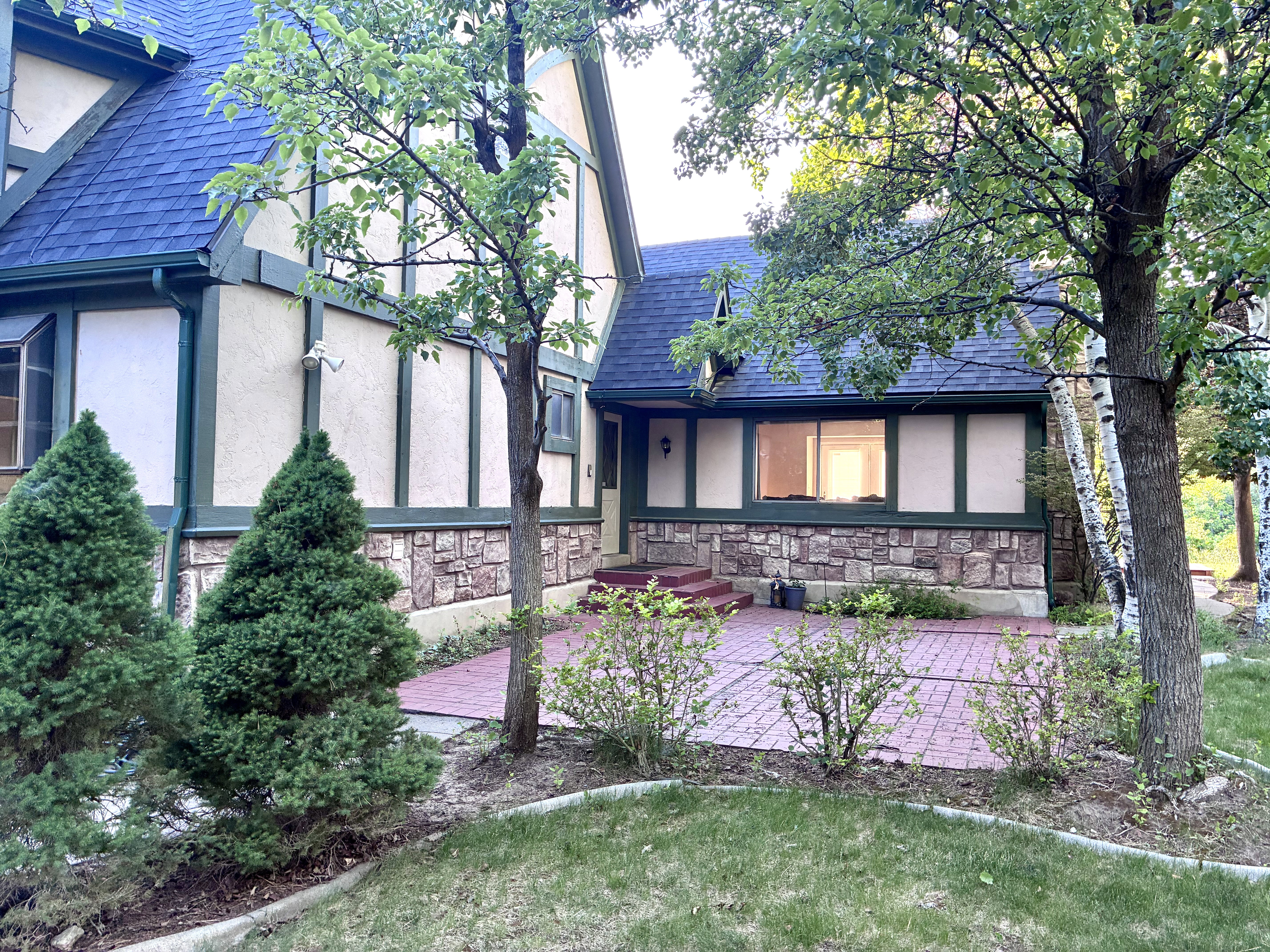 Tudor-style exterior showcasing a dark blue shingle roof, stone foundation, and cream stucco siding with green timber accents