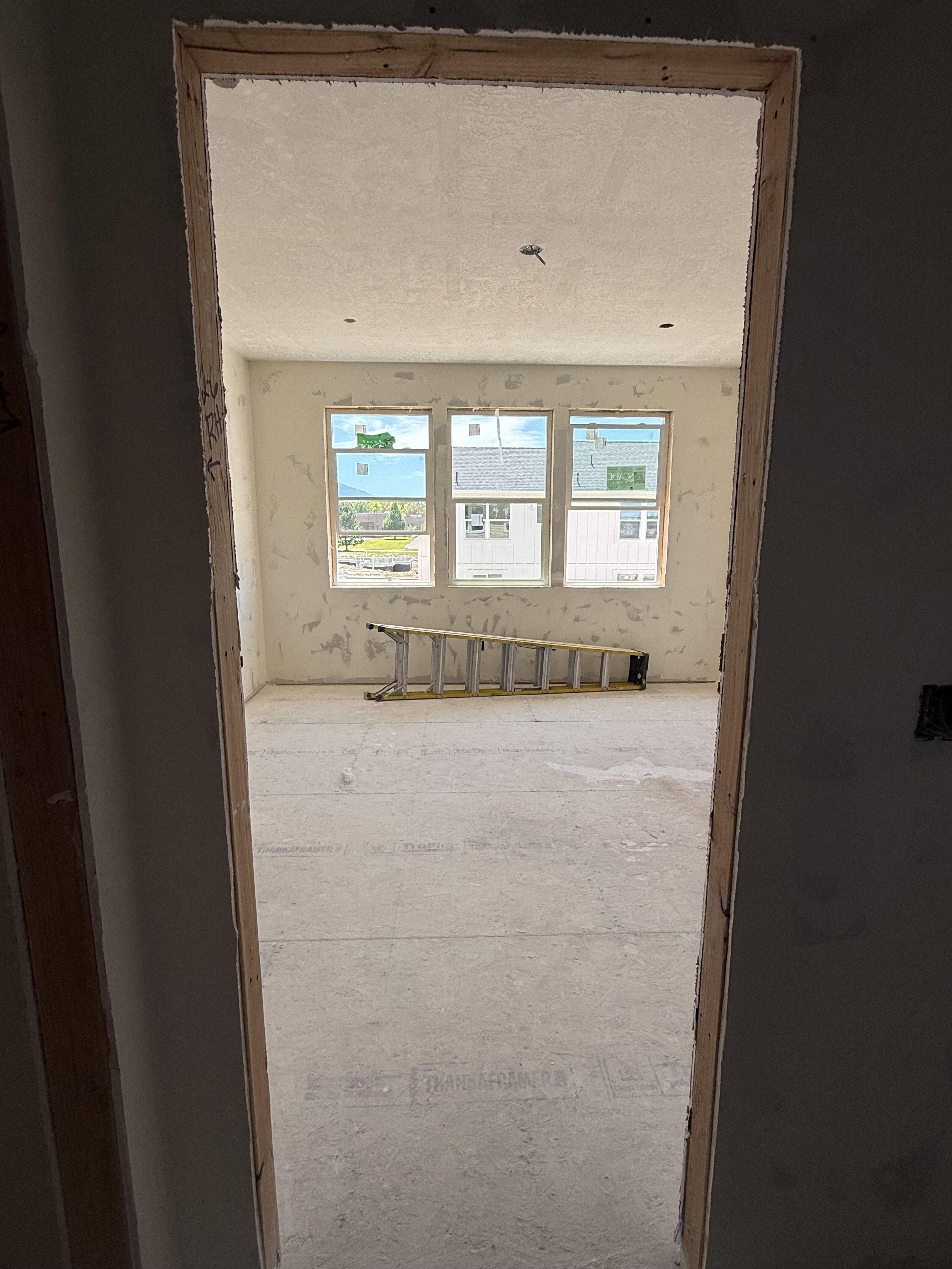 Spacious interior room featuring three large windows, exposed wall framing, concrete subflooring, and a high ceiling