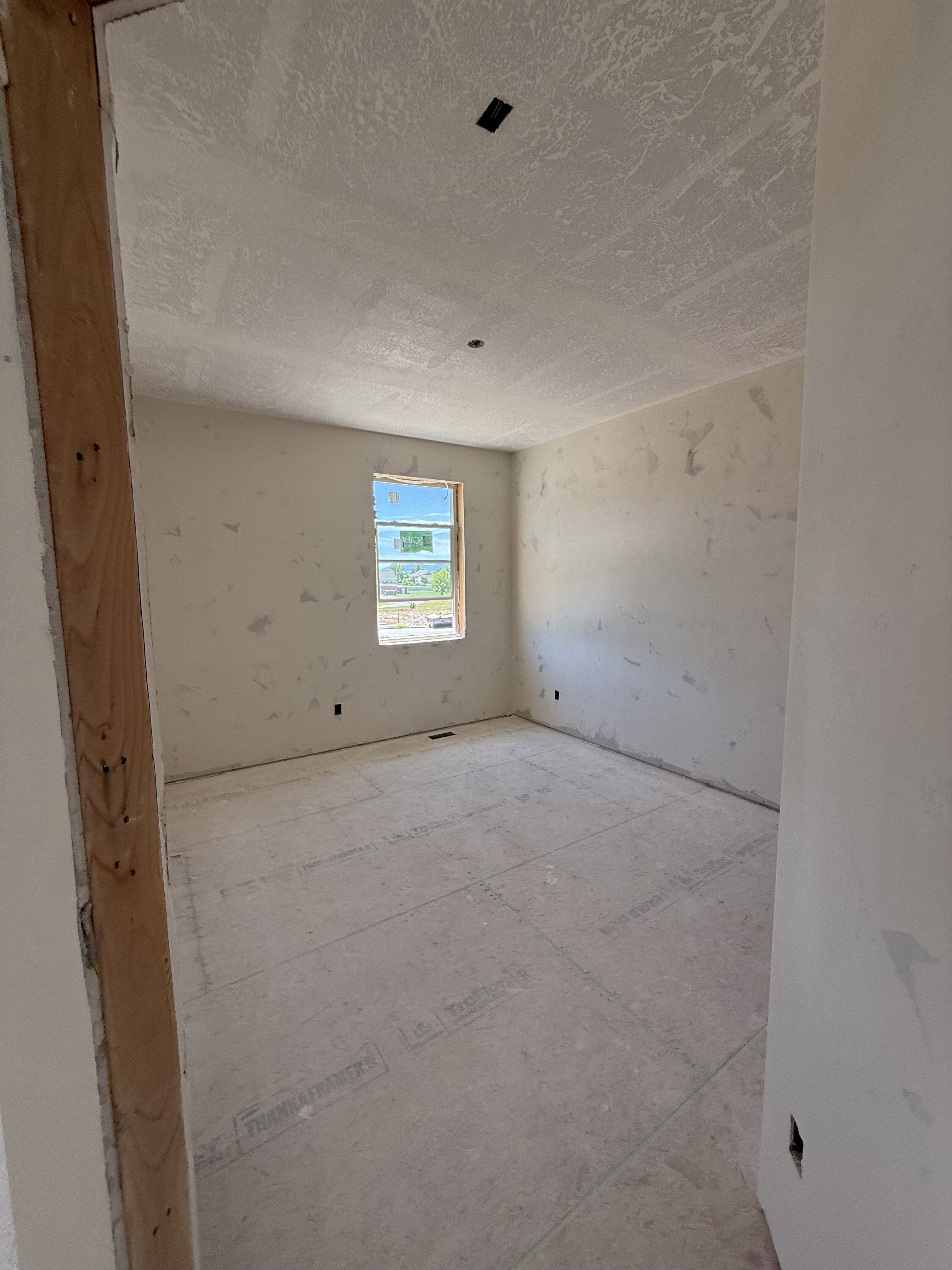 Unfinished interior space featuring a window, textured ceiling, and exposed wall framing
