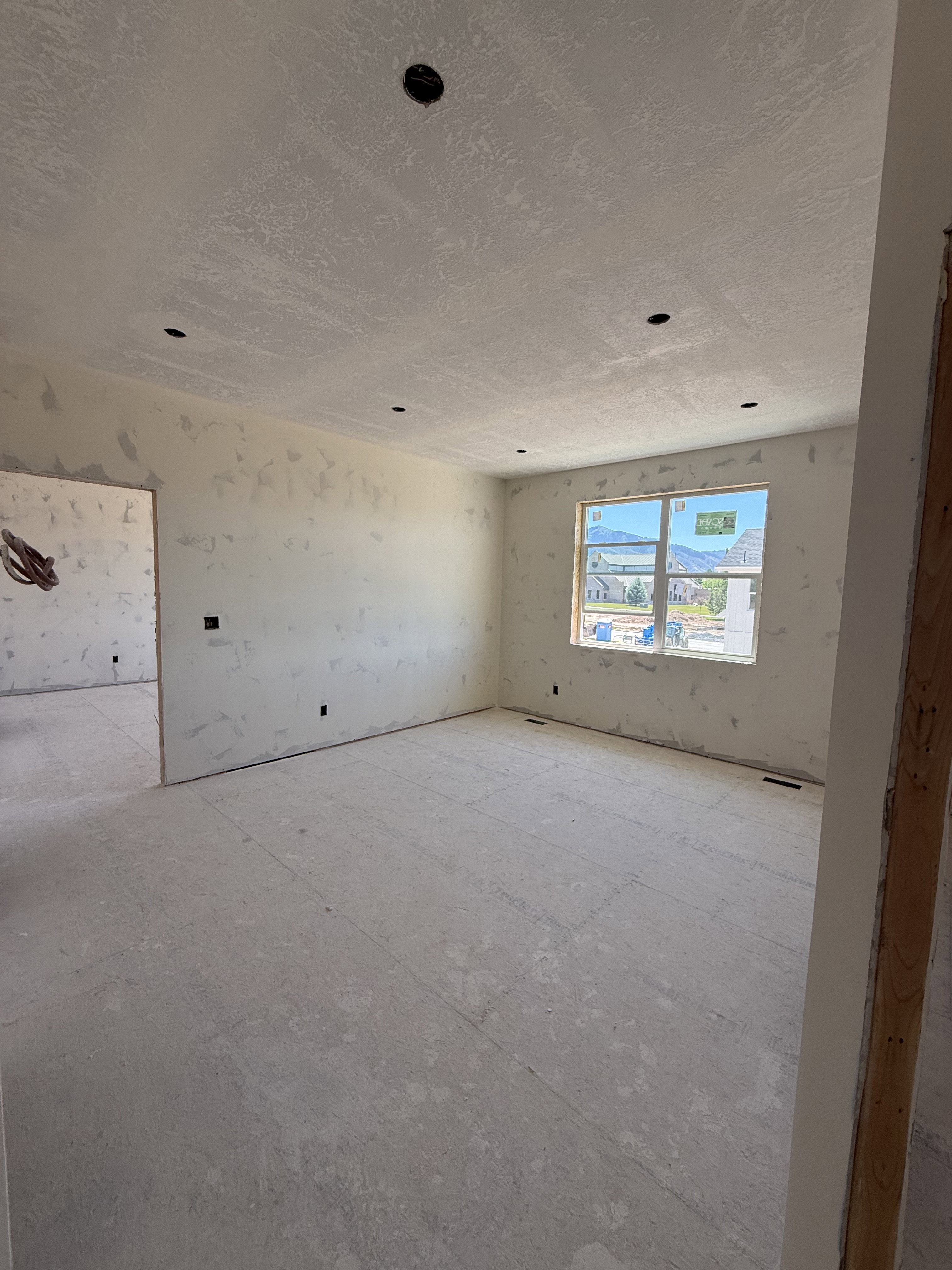 Expansive interior space featuring multiple recessed lighting fixtures, a large window, a prepped wall surface, and a raw subfloor ready for finishing