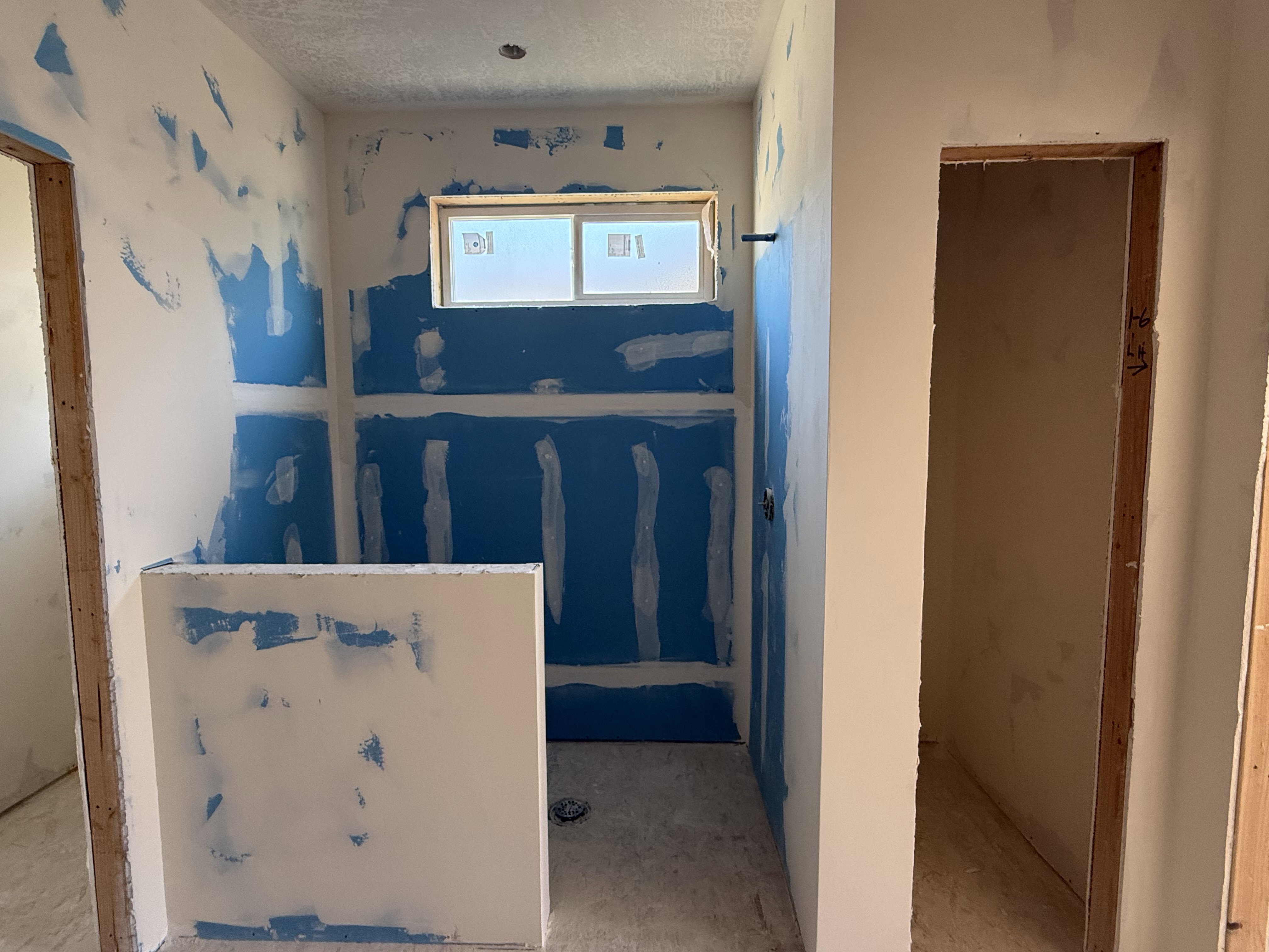 Bathroom space currently under construction, featuring a built-in shower stall with a window, and exposed wall framing