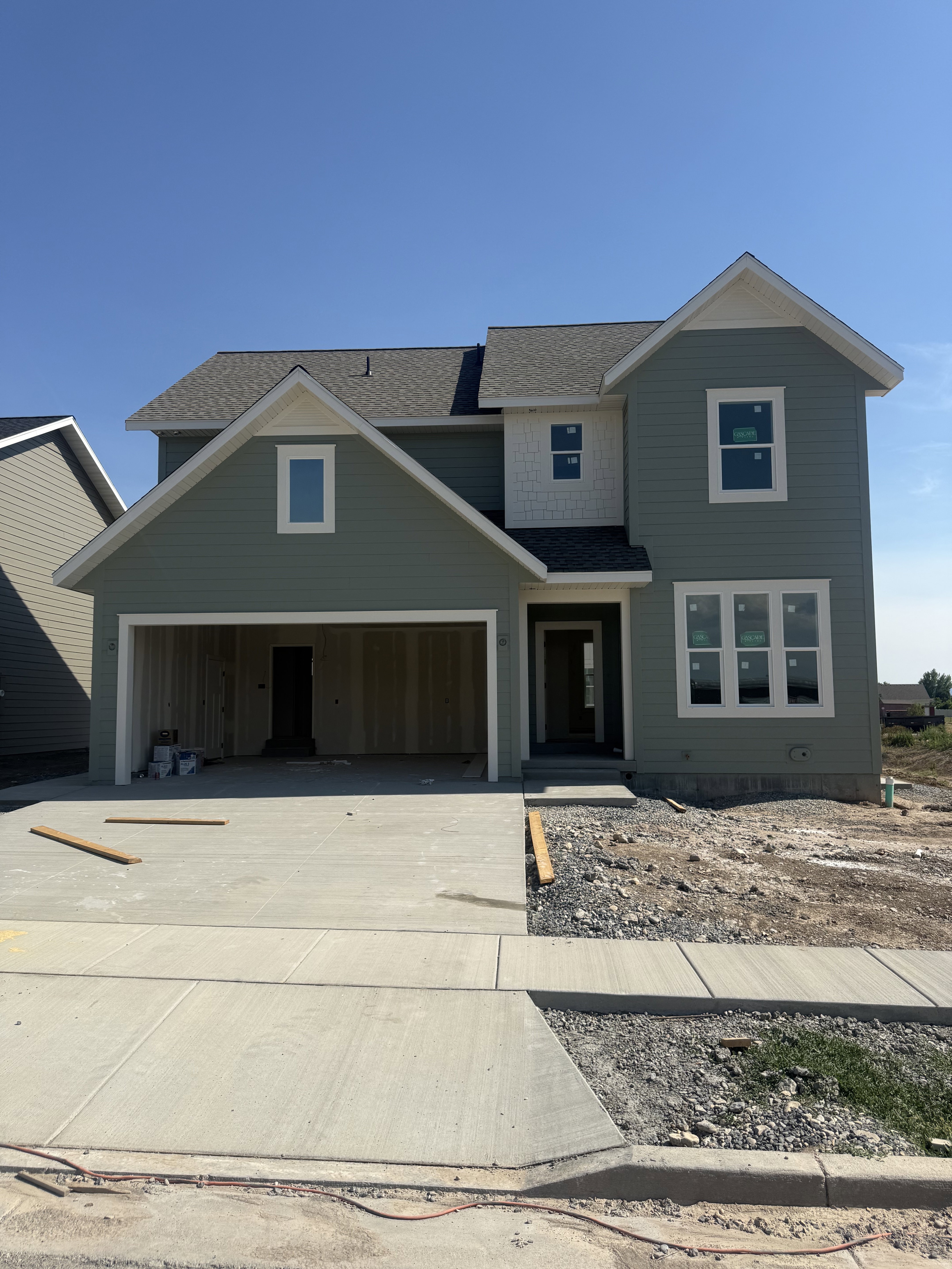 Two-story residence featuring sage green siding, white trim accents, a shingled roof, a two-car garage opening, and a concrete driveway