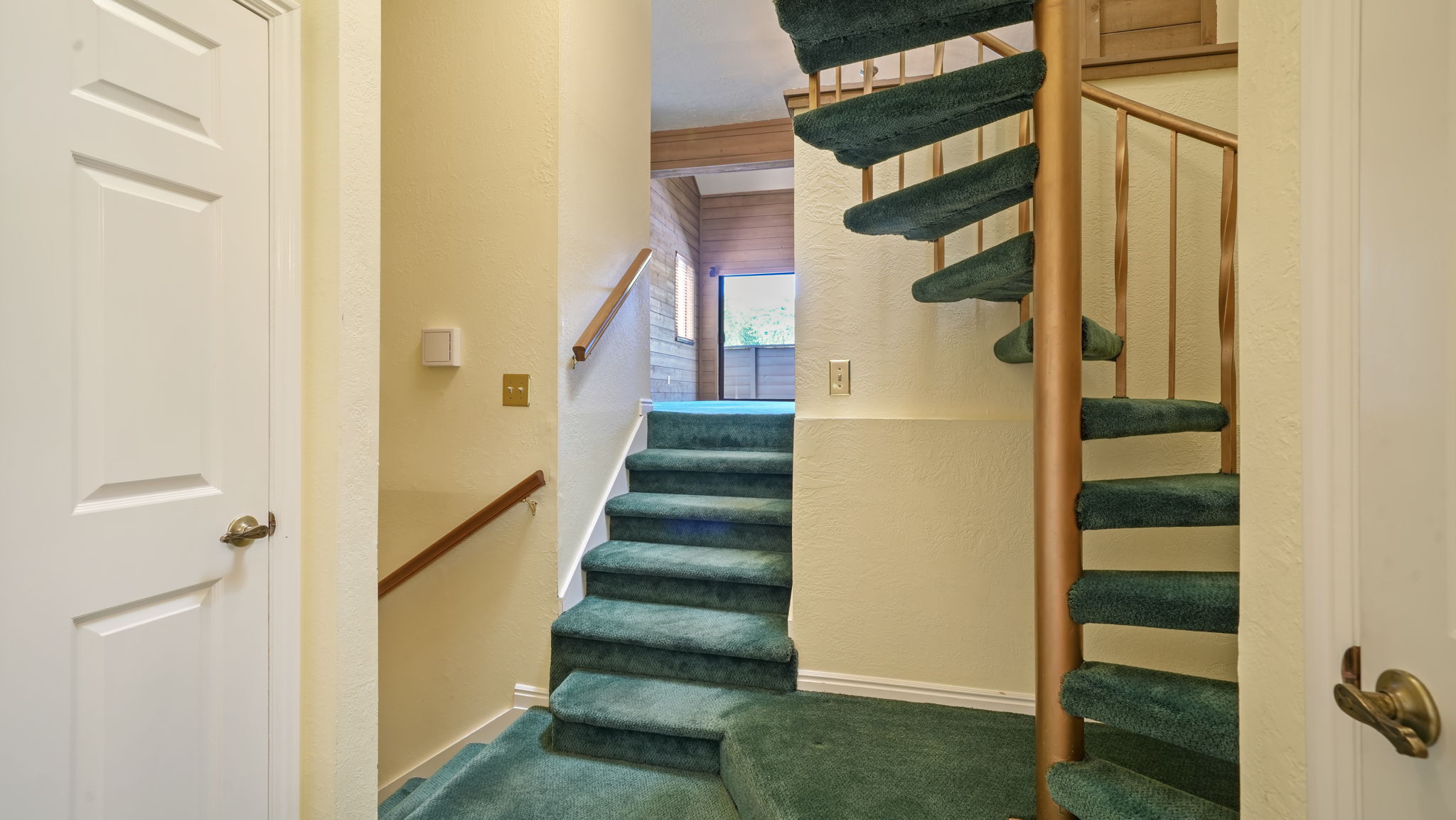 Dual staircase configuration featuring a straight carpeted stairwell with wood railing and a spiral staircase with carpeted treads and a metal banister