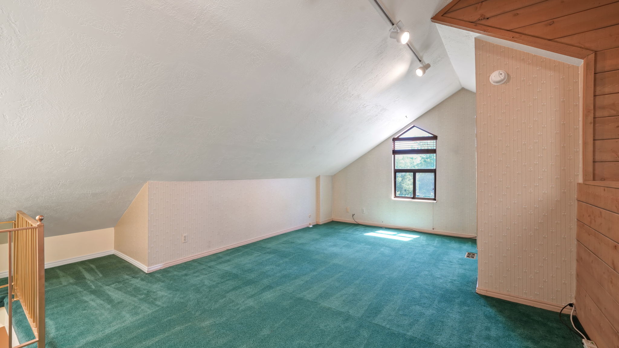 Spacious loft area featuring a peaked ceiling, an angular window, and track lighting
