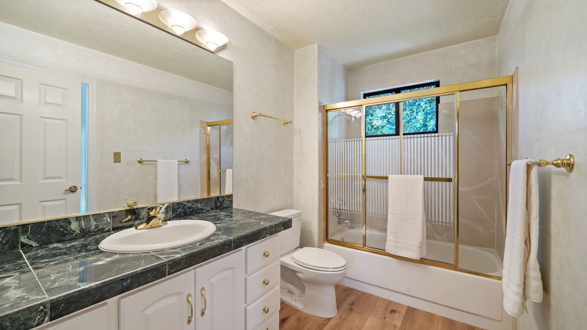 Bathroom featuring a dark stone countertop with integrated sink, white cabinetry, and a gold-framed shower/tub combination with frosted panels