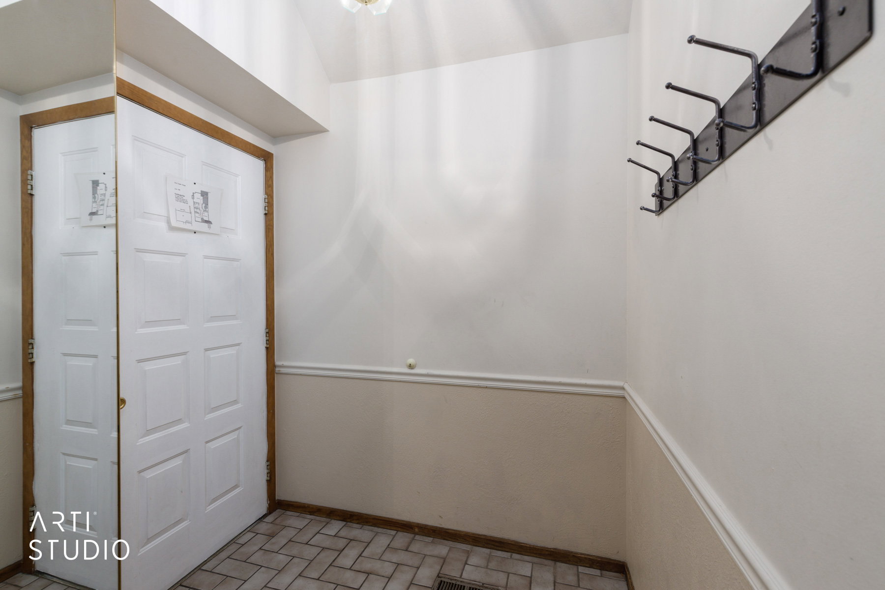 Entryway featuring a paneled door with wood-finish trim, herringbone tile flooring, wainscoting, and a wall-mounted coat rack