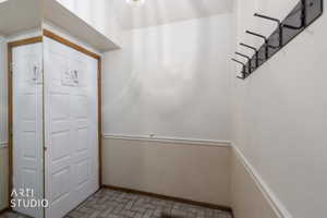 Entryway featuring a paneled door with wood-finish trim, herringbone tile flooring, wainscoting, and a wall-mounted coat rack