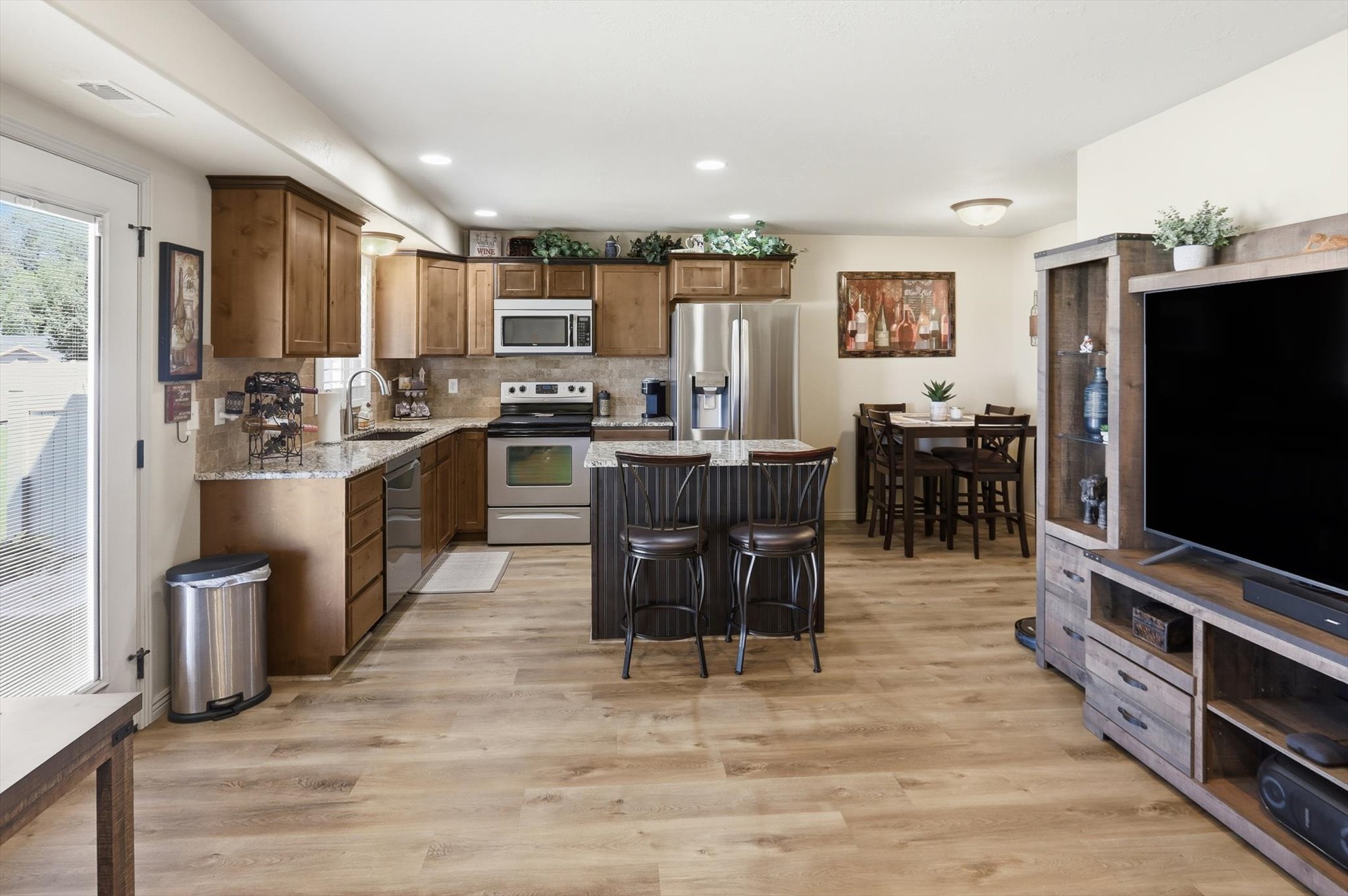 Open-concept living space featuring wood-finish flooring, a kitchen with wood cabinetry and stainless steel appliances, granite countertops, and a central kitchen island