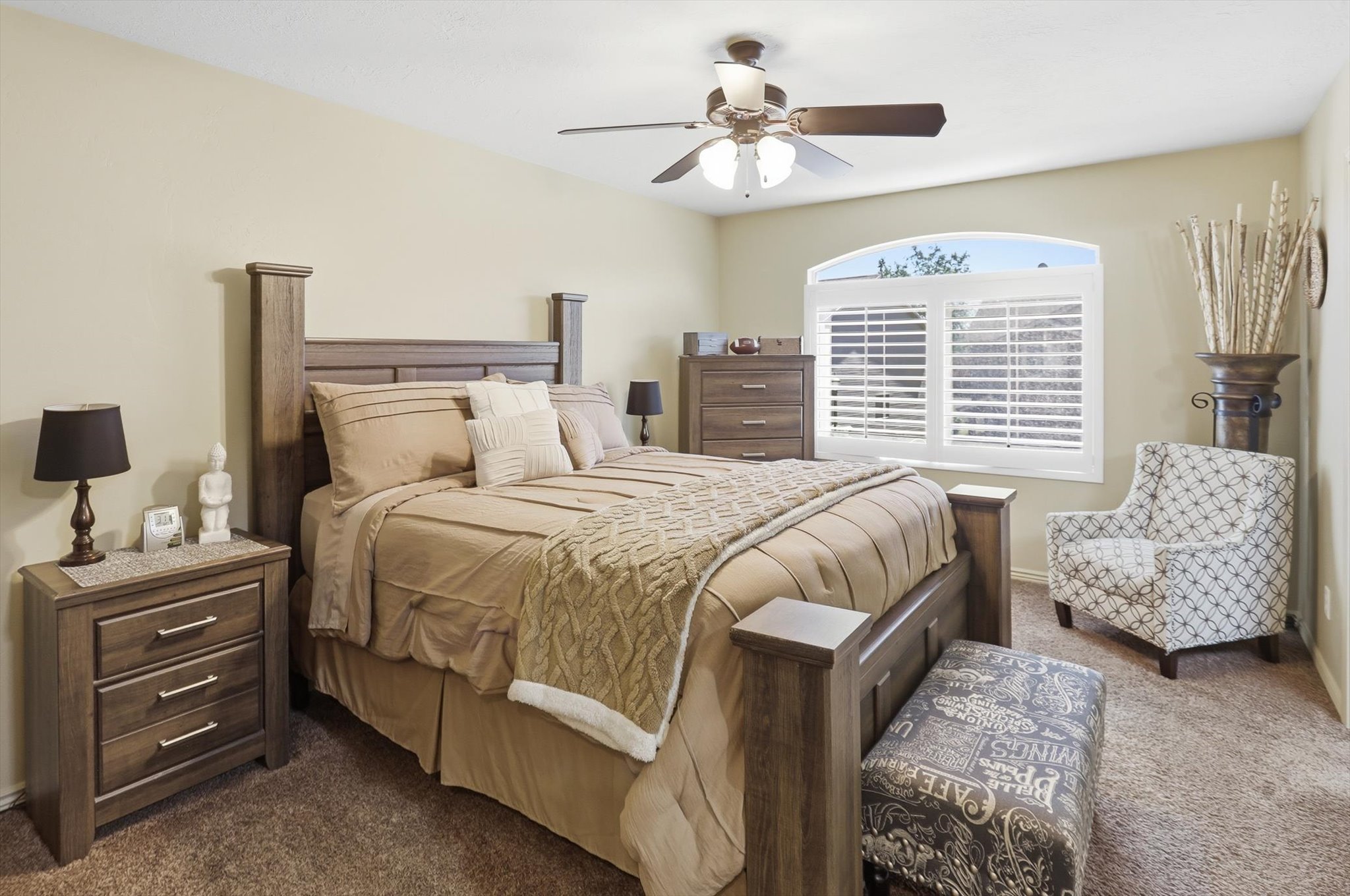 Carpeted bedroom featuring a ceiling fan with integrated lighting, a window with an arched transom, and white plantation shutters