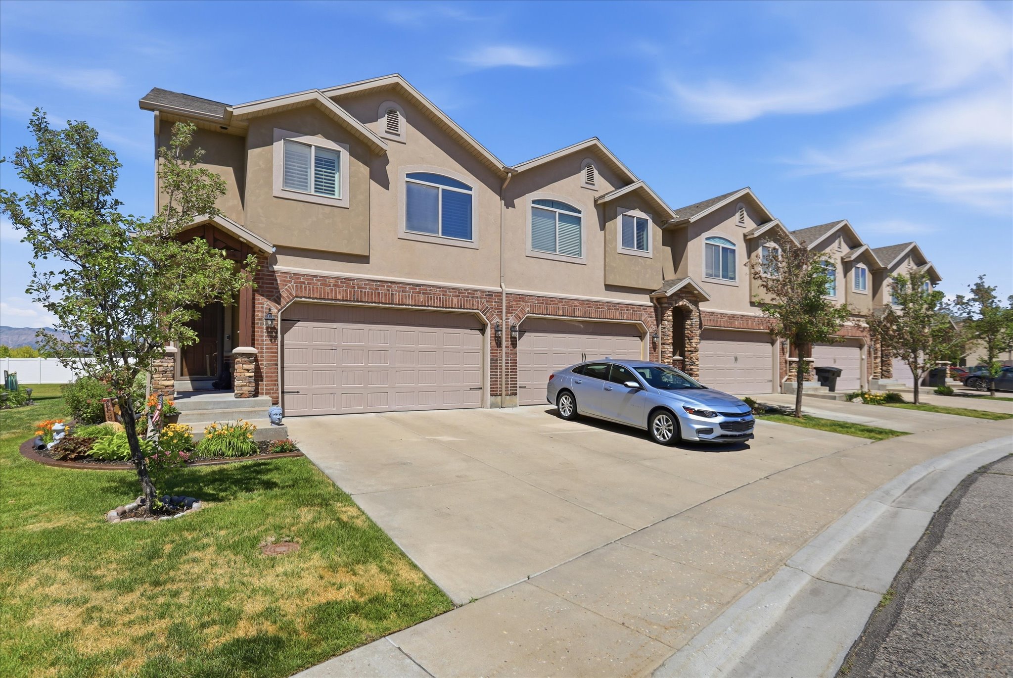 Contemporary townhome exterior featuring stucco and brick accents, an attached two-car garage, and a covered entry with stone pillars