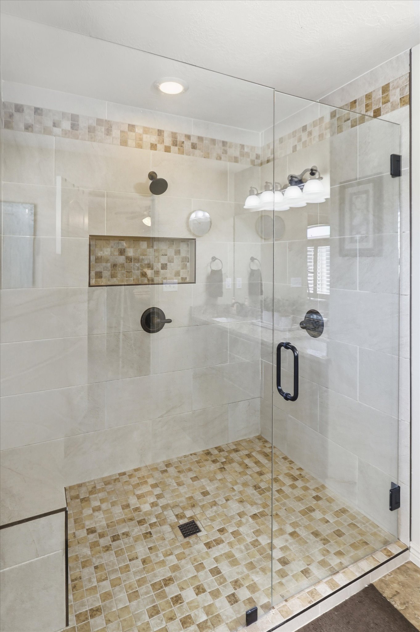 Glass-enclosed shower featuring large format wall tiles, a mosaic tile floor, and a recessed shower niche