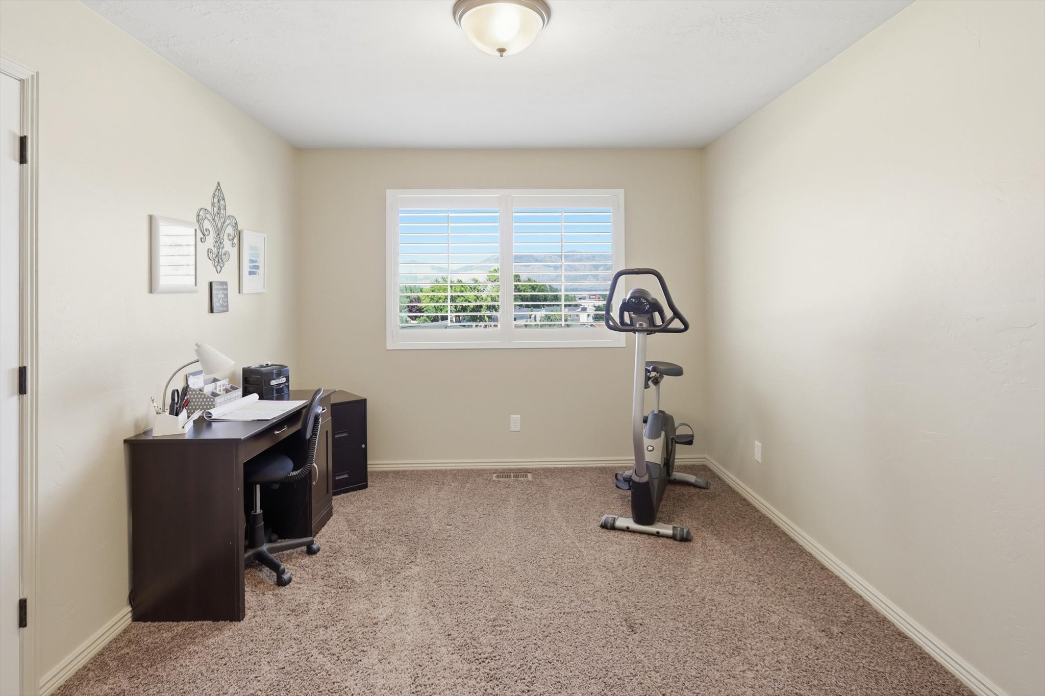 Neutral-toned room featuring light beige walls and a window with white plantation shutters