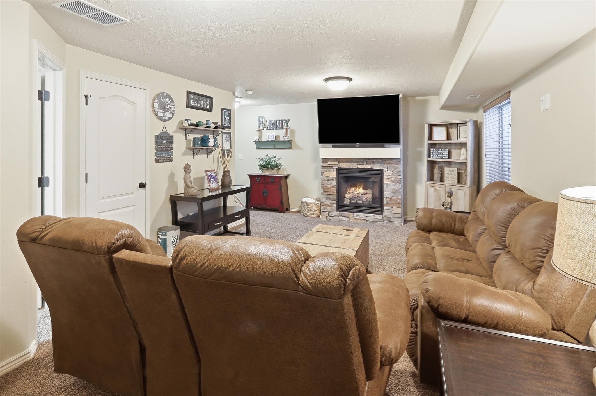 Carpeted living space featuring a stacked stone fireplace with a mounted television above
