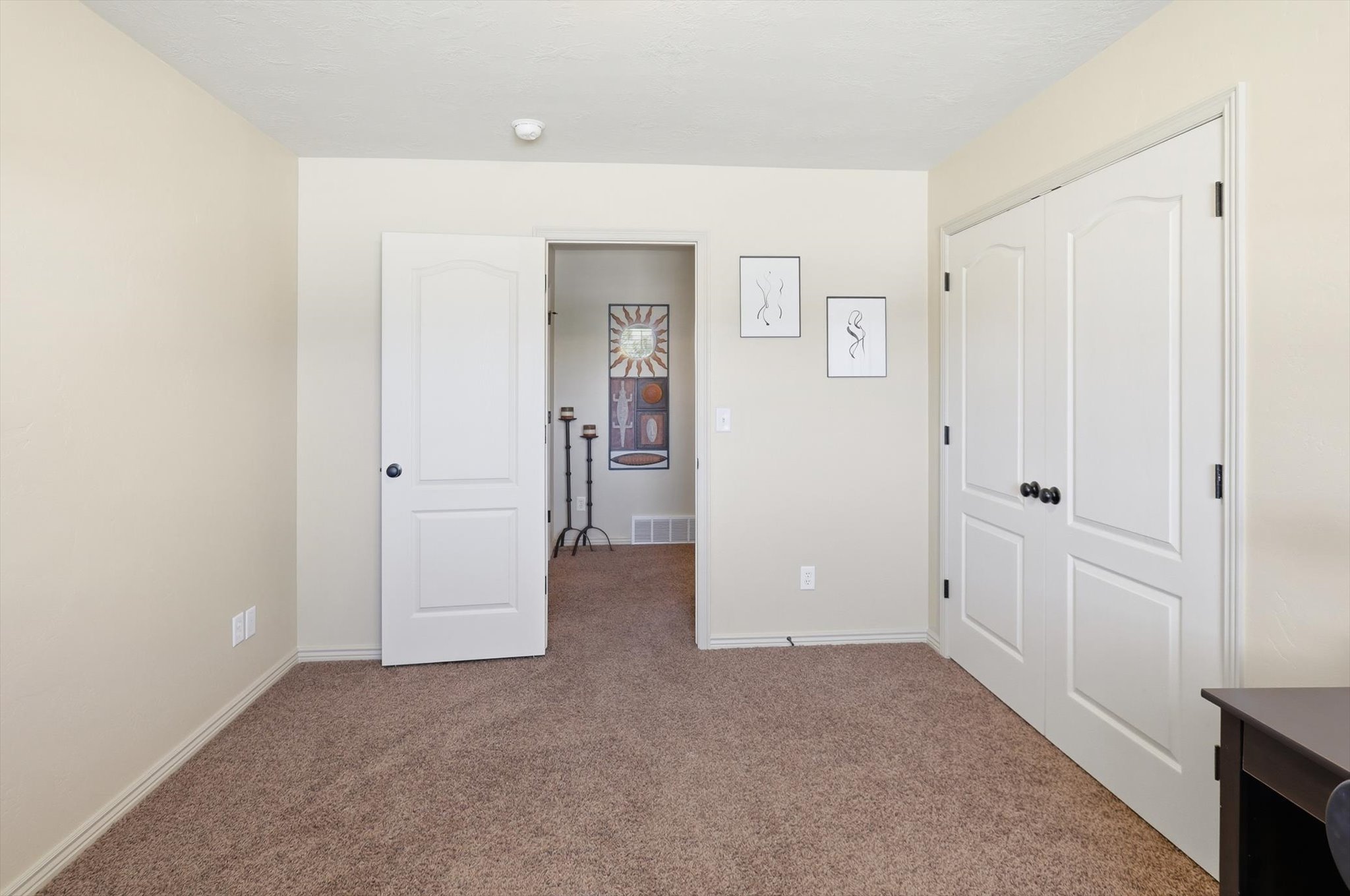 Carpeted interior room featuring neutral wall tones, white trim, a white interior door with dark hardware, and a white bi-fold closet door with dark hardware