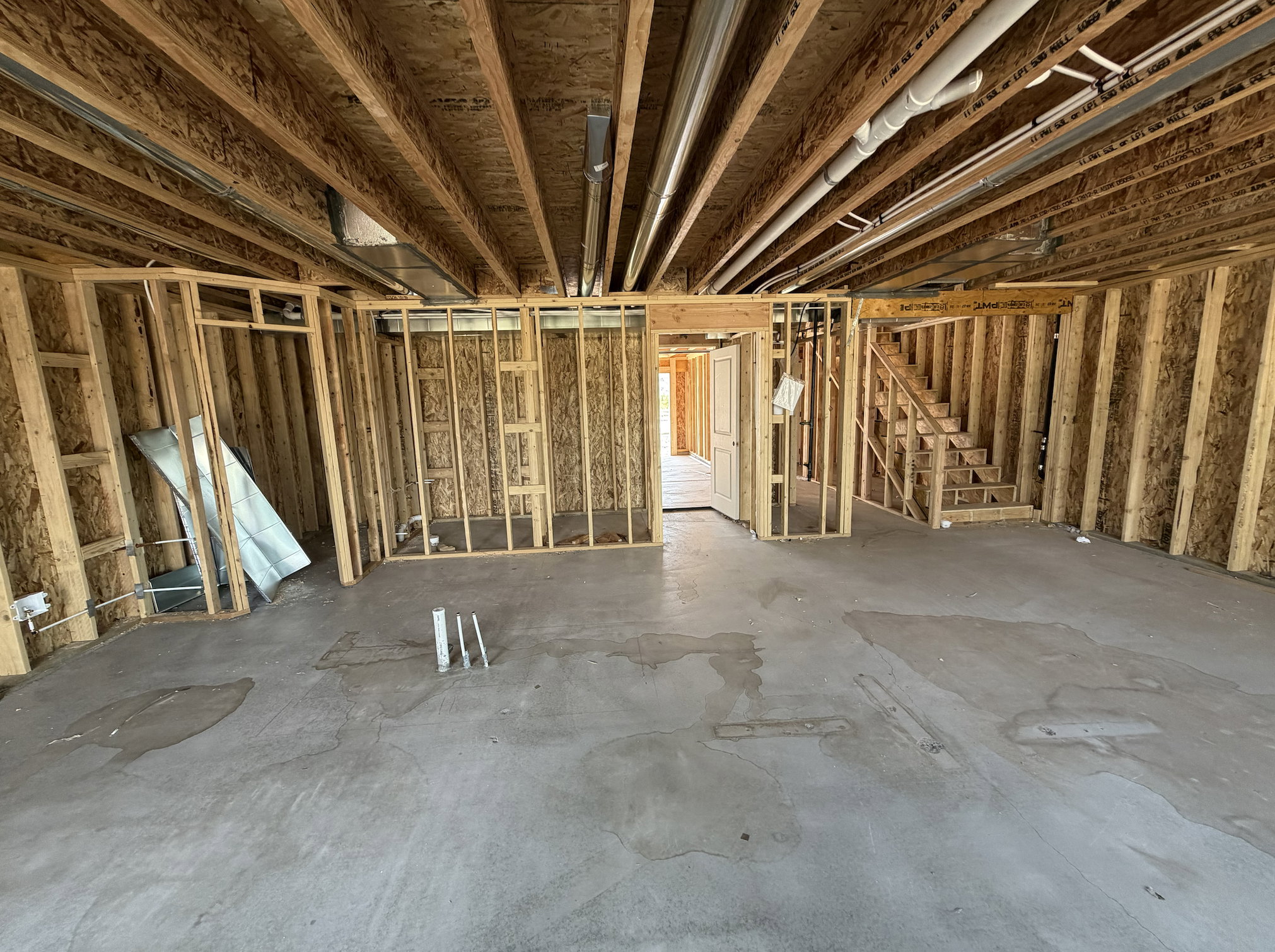 Unfinished basement featuring extensive framing, exposed ceiling joists, concrete flooring, and a visible staircase structure