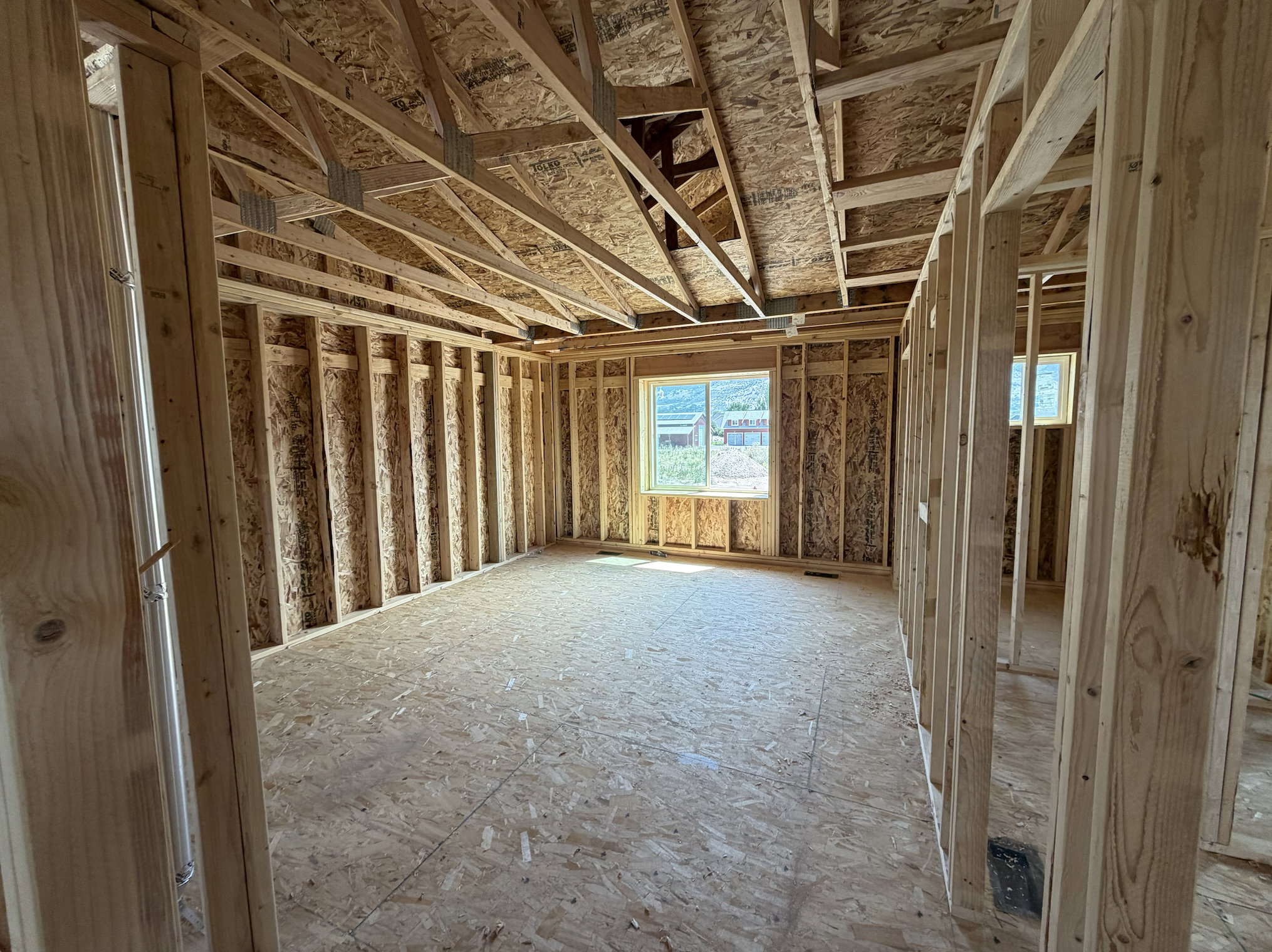 Unfinished interior space featuring exposed wood framing, oriented strand board subflooring, and a vaulted ceiling with visible trusses