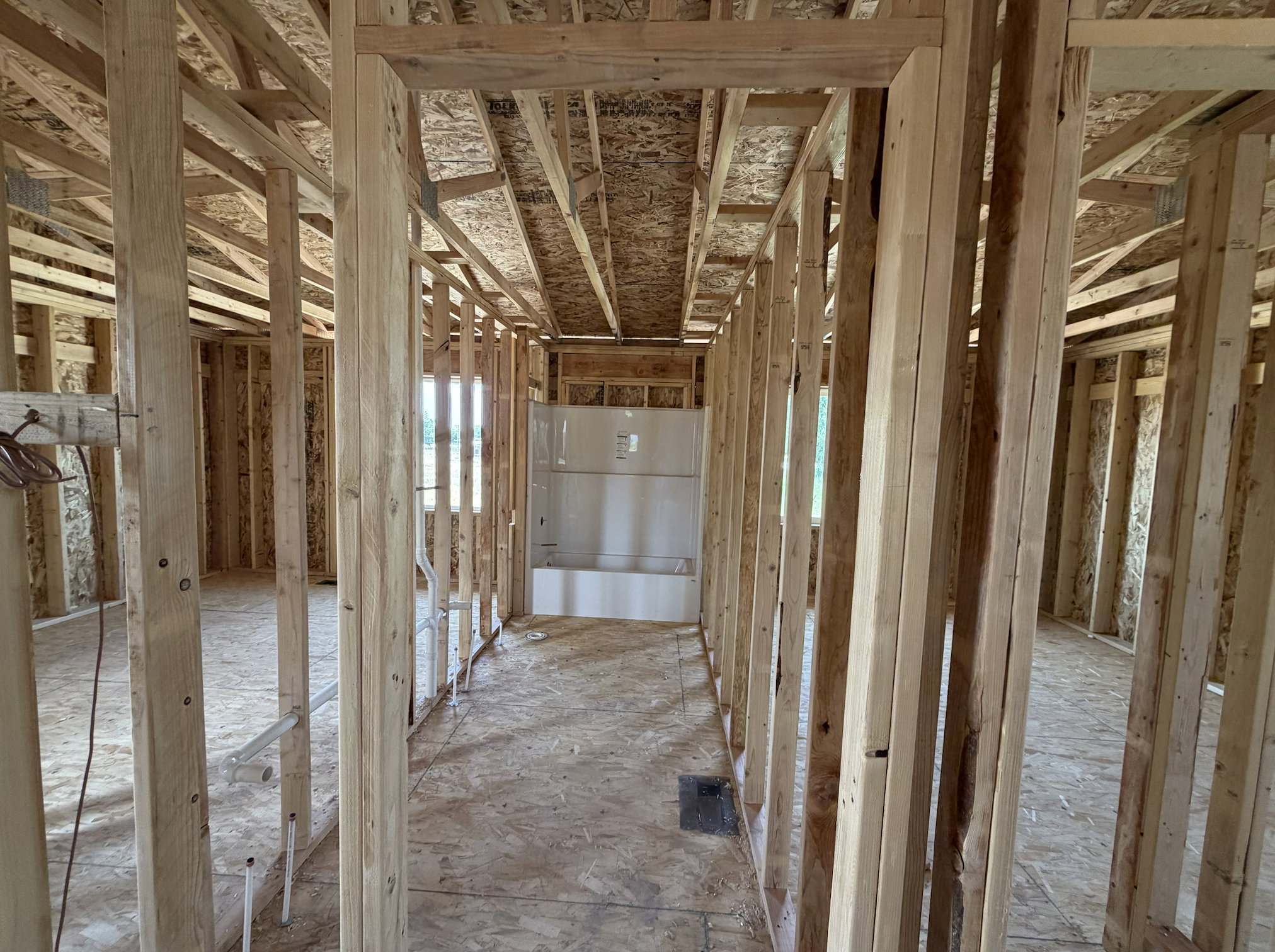 New construction framing featuring a visible bathtub installation, wood framing, oriented strand board subfloor, and exposed plumbing lines