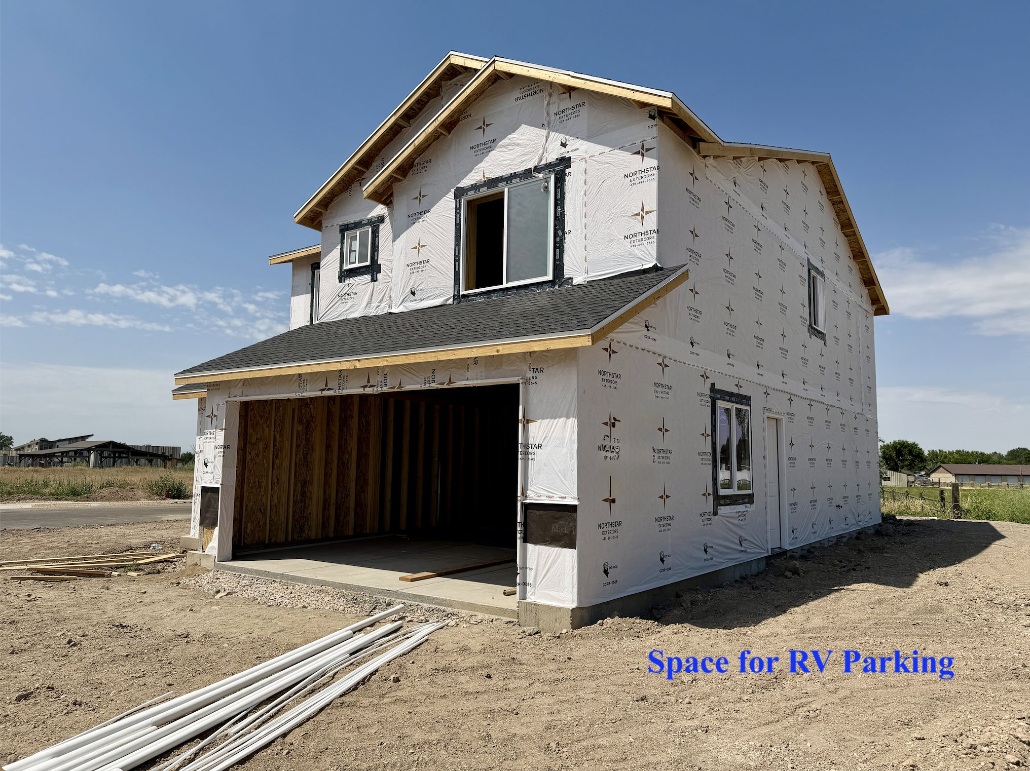 Two-story construction featuring an attached garage with concrete flooring, a dark shingle roof, and a gravel side area