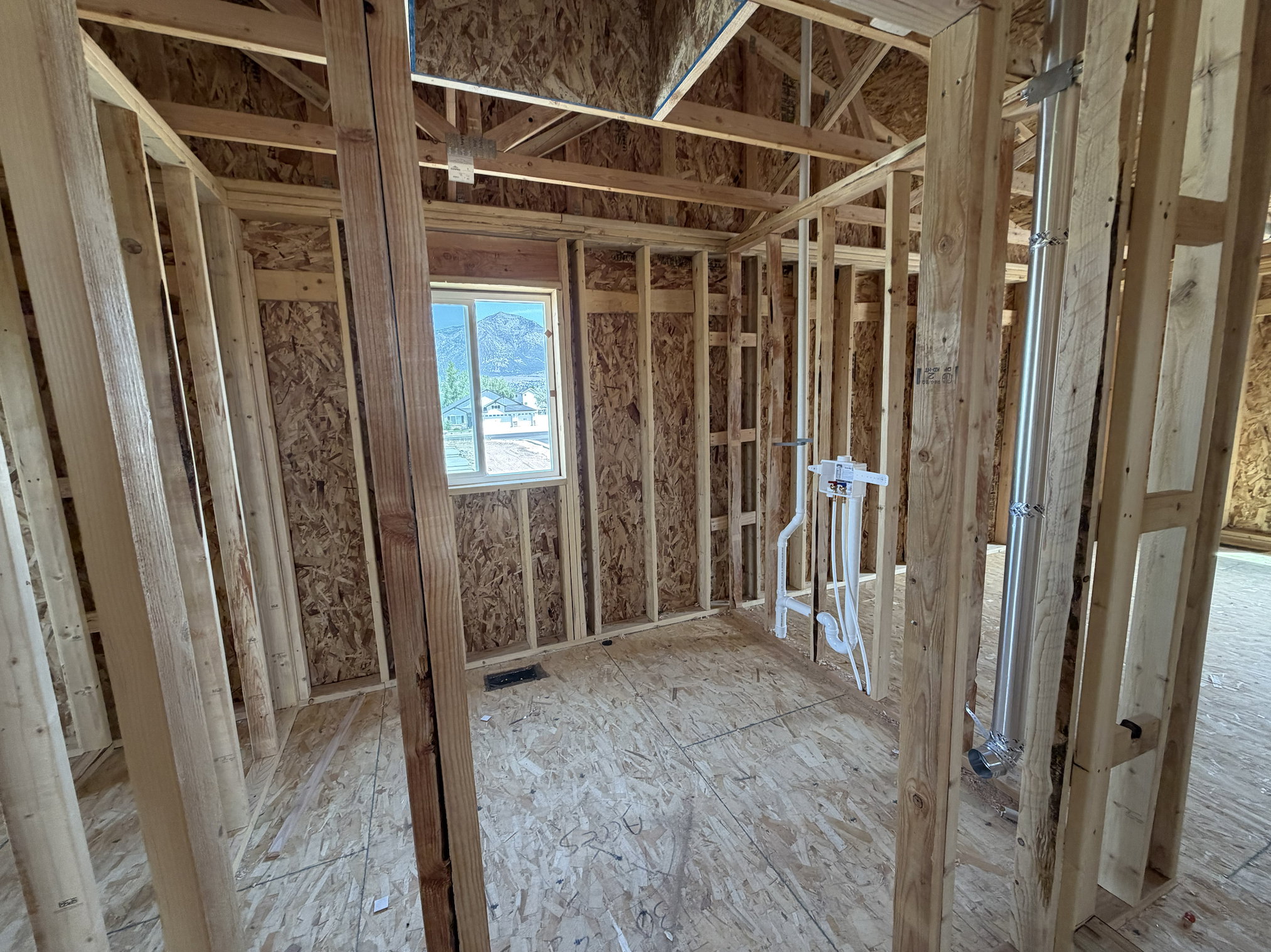 Framed interior space featuring visible plumbing rough-in, a window, and exposed wood framing