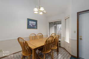 Dining area featuring a vaulted ceiling, patterned tile flooring, and wainscoting