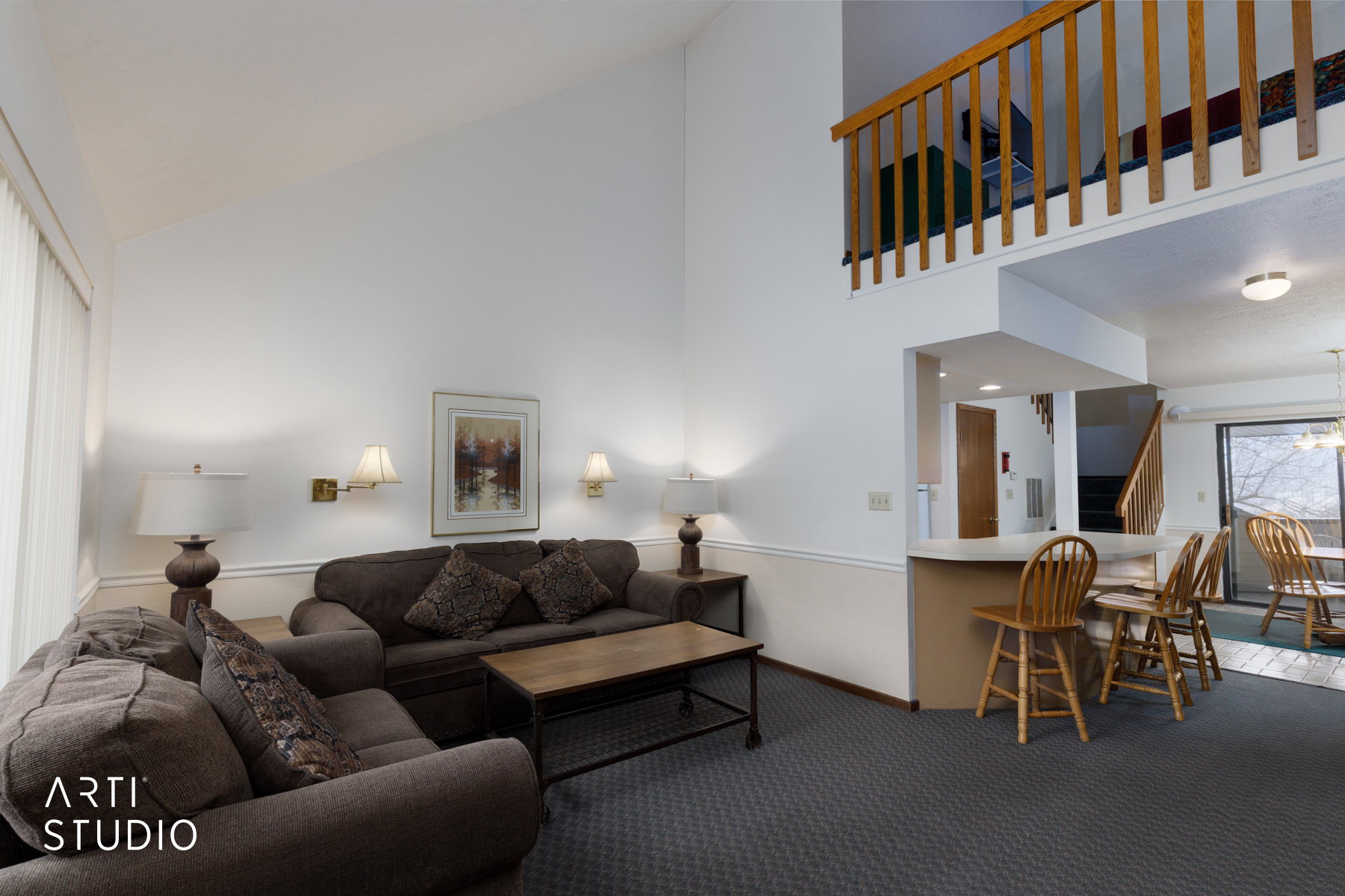 Vaulted ceiling living area featuring a wood railing loft, neutral wall paint, and wall sconce lighting