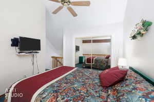 Vaulted ceiling bedroom with a ceiling fan, wall-mounted television, and mirrored closet doors