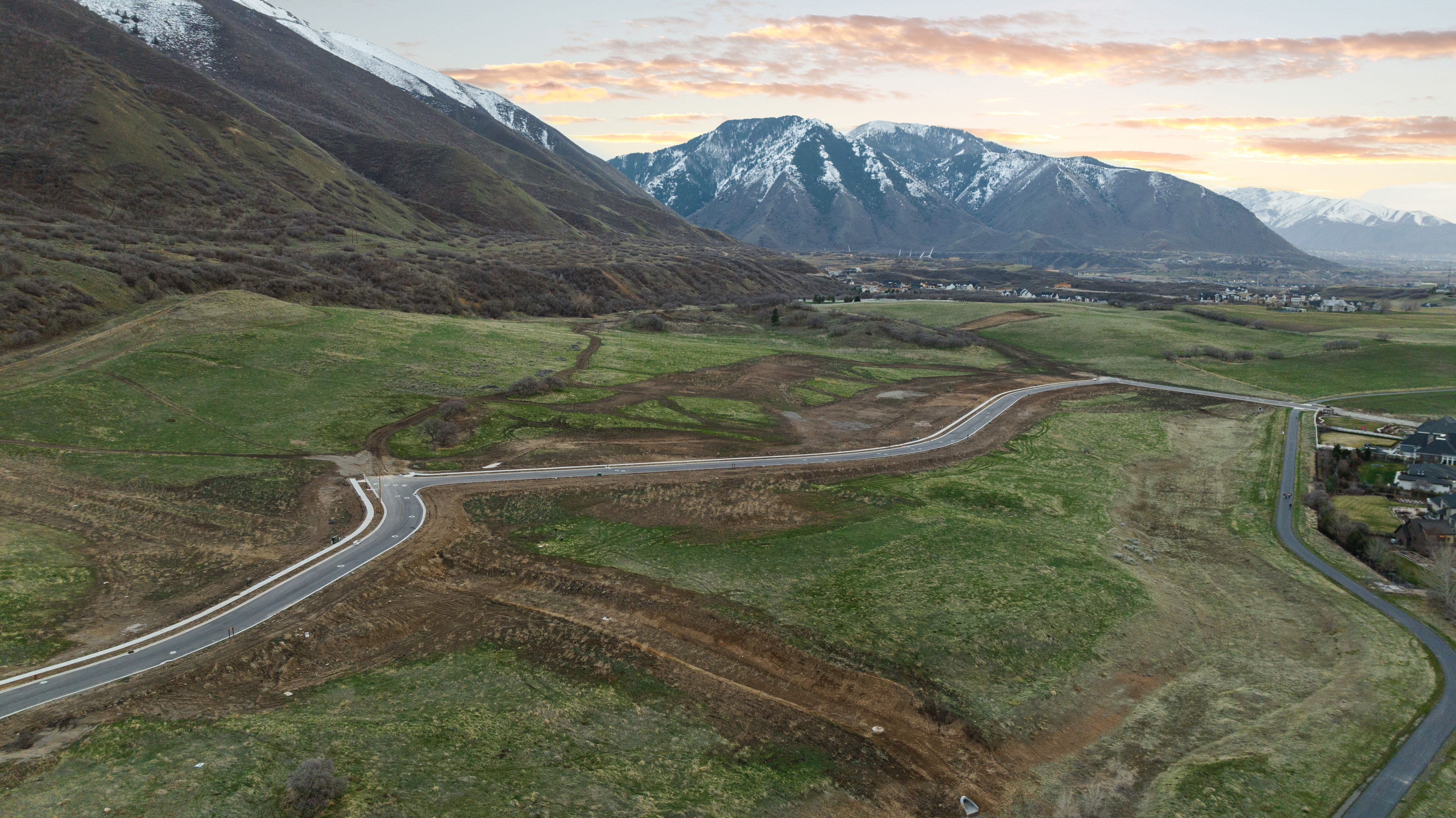 Expansive undeveloped land featuring paved roads, mountainous backdrop, and established residential areas in the distance
