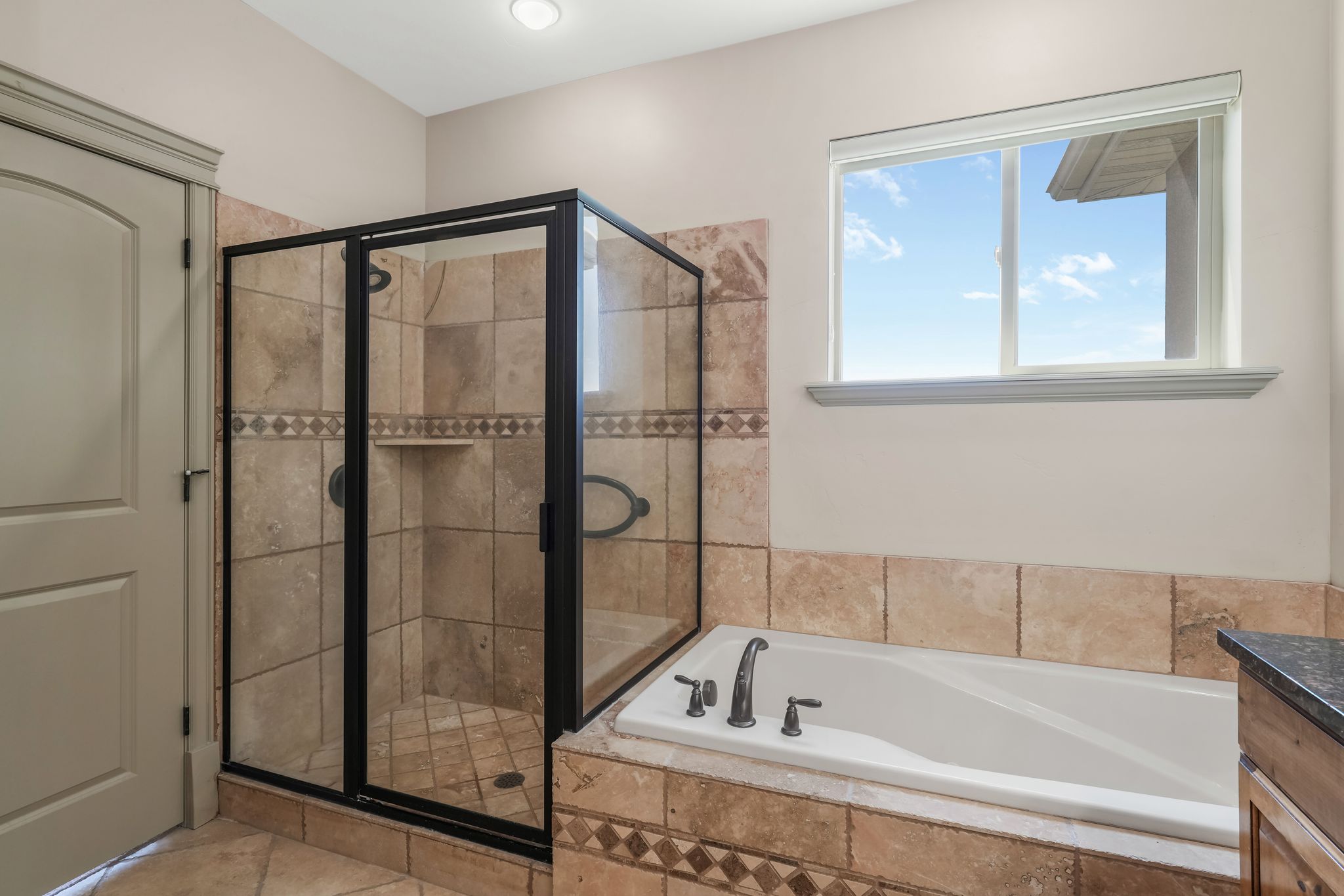 Spacious bathroom featuring a glass-enclosed shower with tile surround, an adjacent built-in soaking tub, and a window with natural light