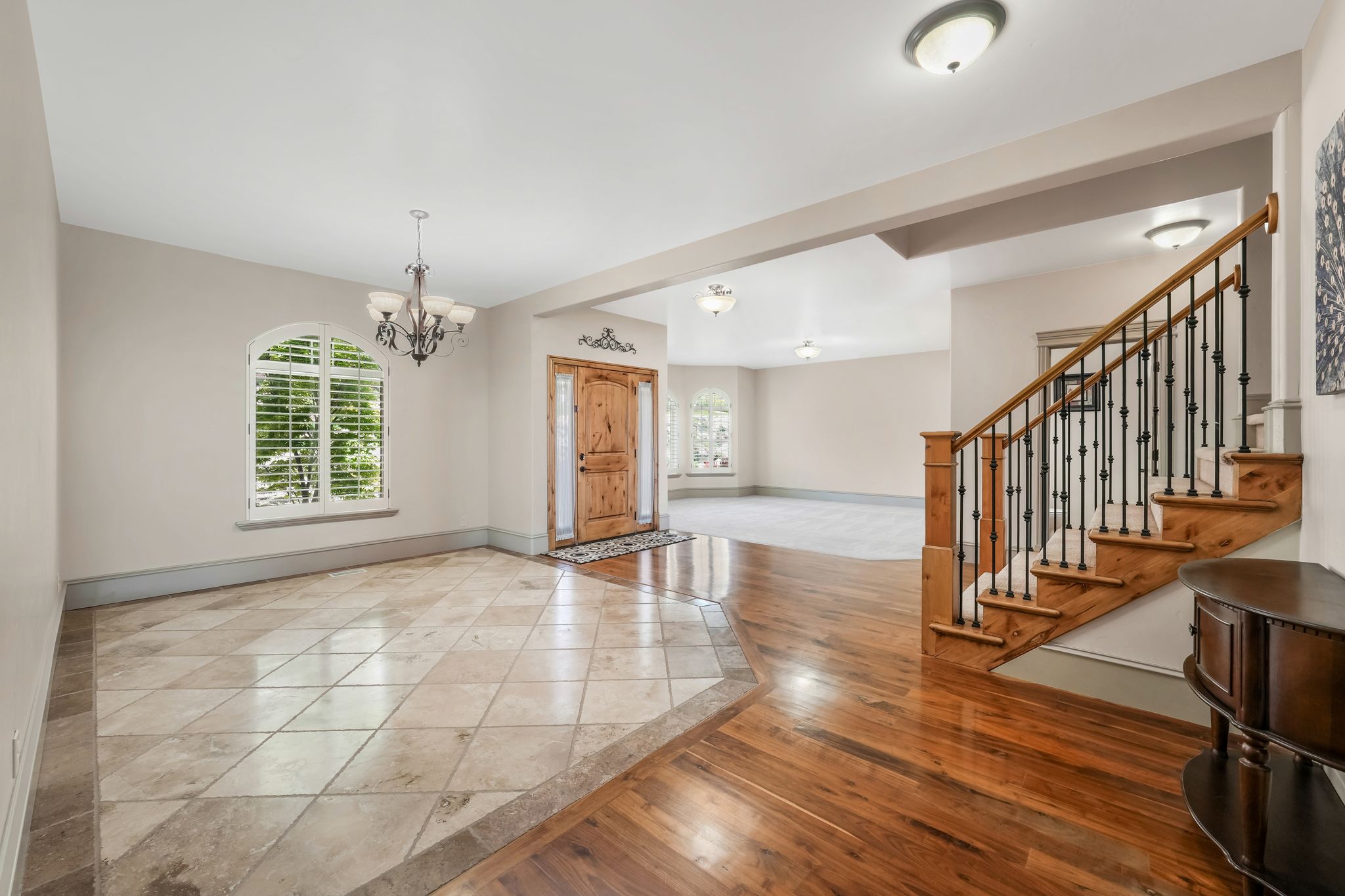 Inviting entryway featuring a wood-finish front door with decorative trim, a grand staircase with wrought iron balusters, and a combination of tile flooring and polished wood-finish flooring