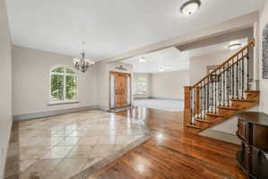 Inviting entryway featuring a wood-finish front door with decorative trim, a grand staircase with wrought iron balusters, and a combination of tile flooring and polished wood-finish flooring