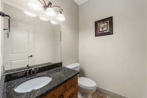 Powder room featuring a wood-finish vanity with an undermount sink, a dark speckled countertop, and a bronze-finish vanity light fixture