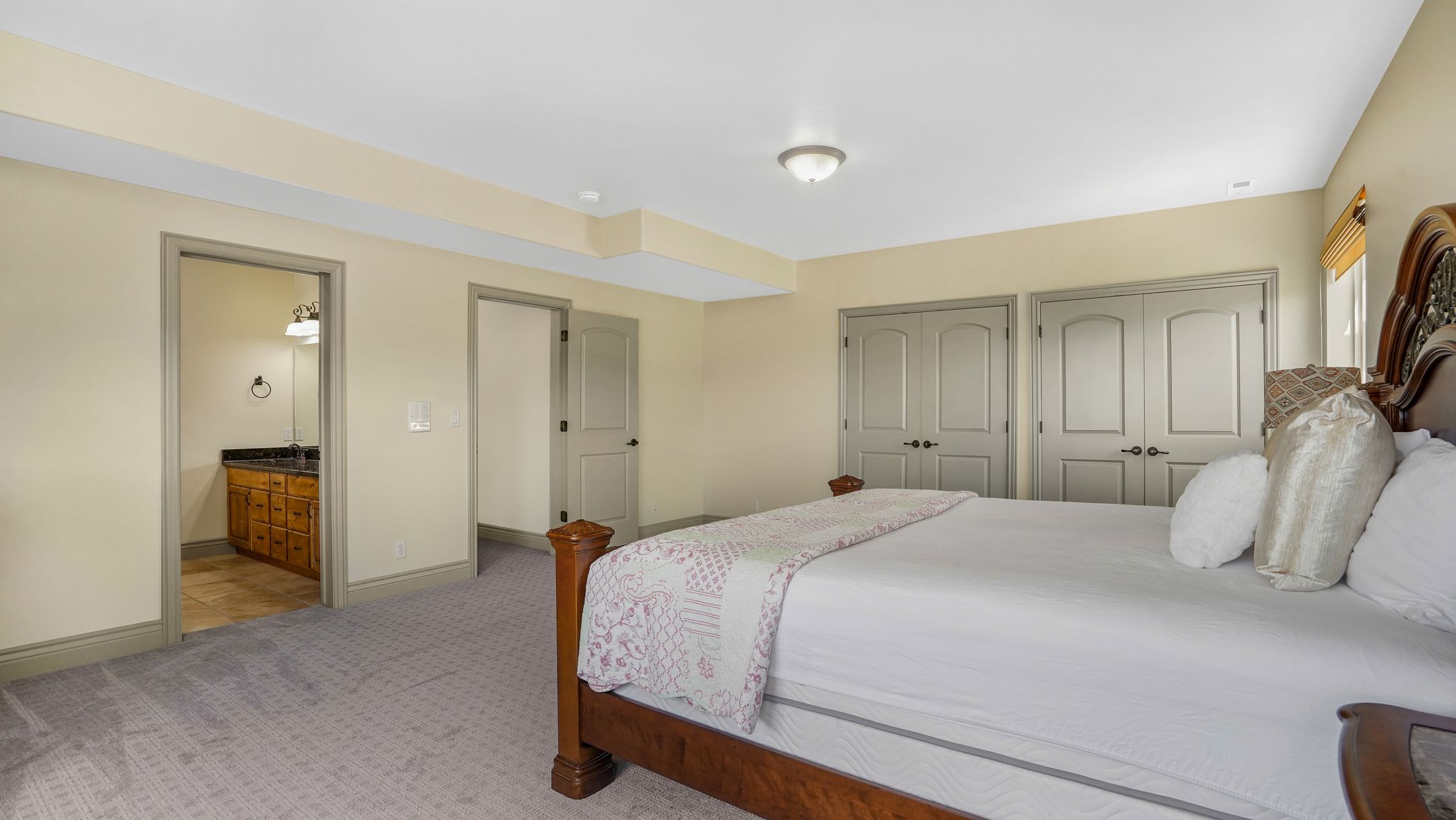 Carpeted bedroom featuring two paneled closet doors, recessed ceiling detail, and a window with blinds