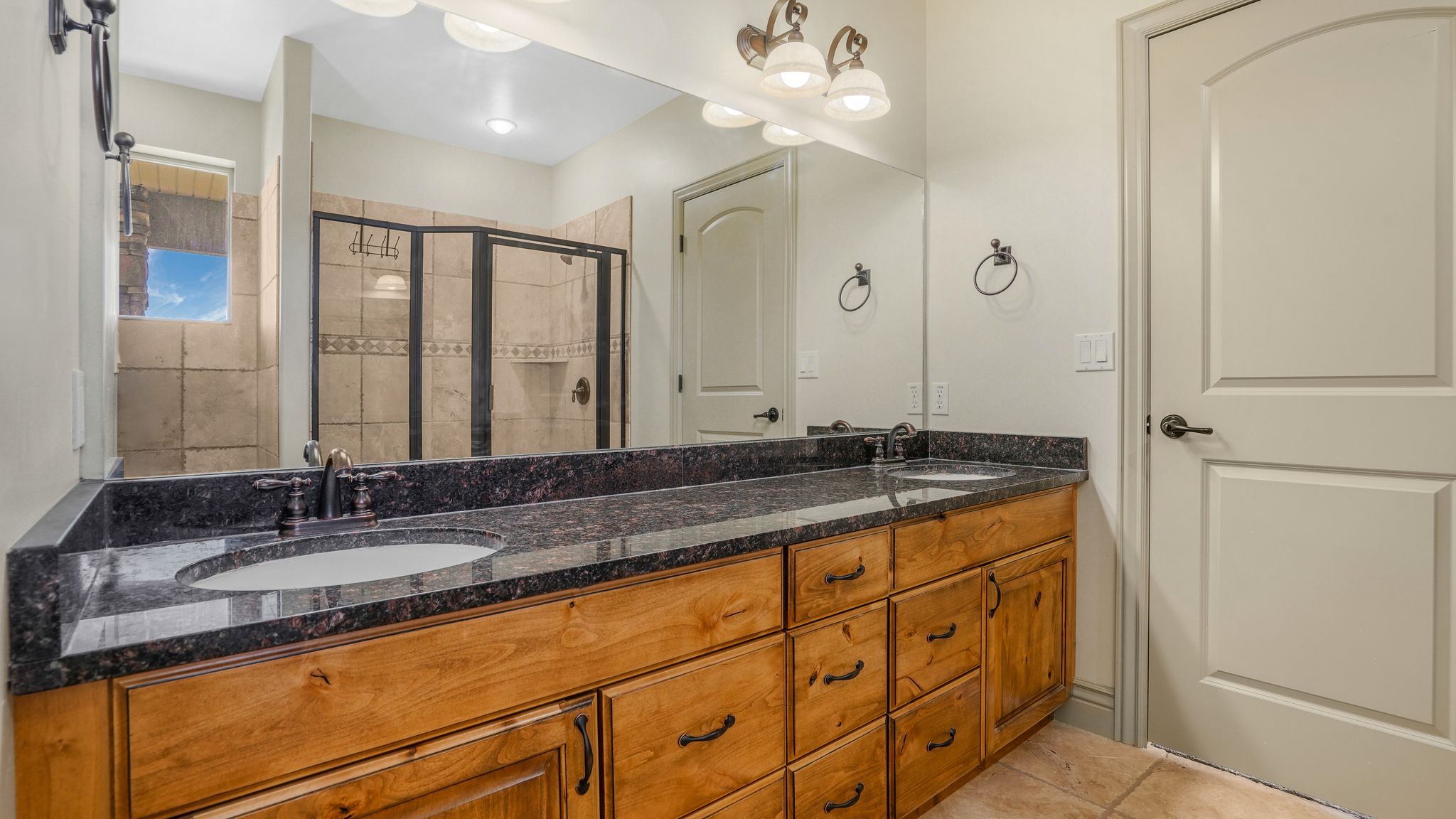 Dual vanity featuring a dark granite countertop and light wood cabinetry with dark hardware