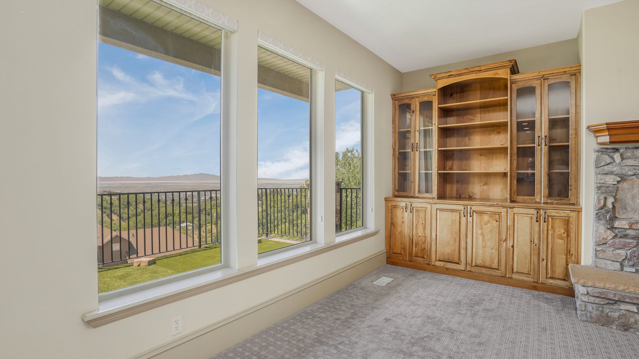 Expansive windows offering distant mountain and valley scenery, custom built-in wood cabinetry with glass-front display cases, integrated wood shelving, and a stone fireplace surround with a hearth