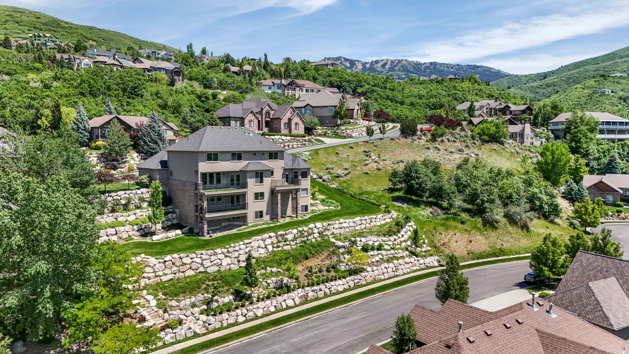 Multi-story residence featuring a tiered landscape design with stone retaining walls