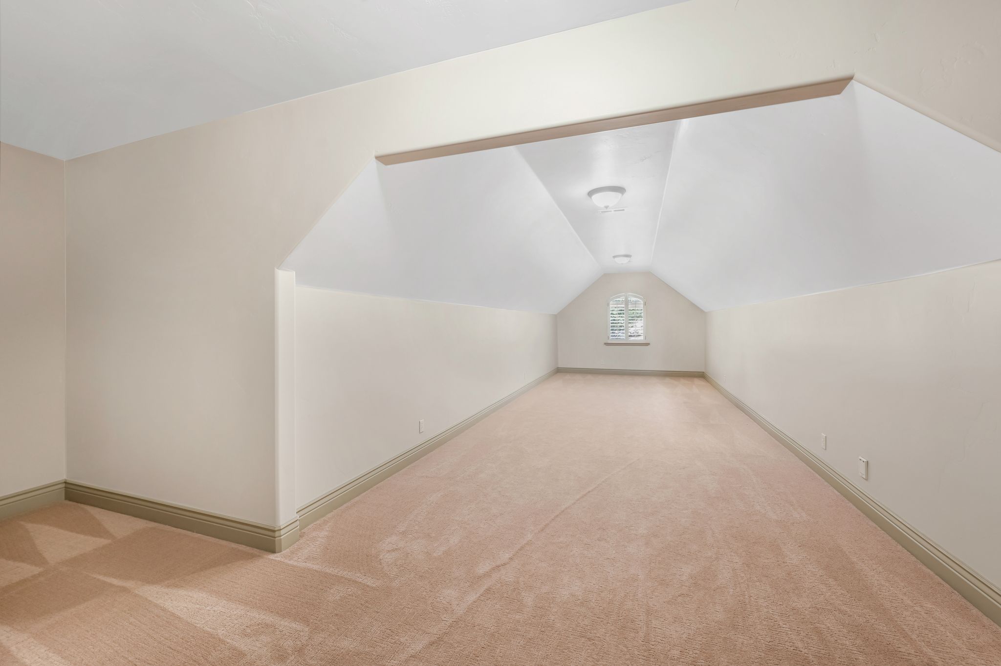 Expansive room featuring sloped ceilings, neutral-toned carpeting, and a central arch-top window