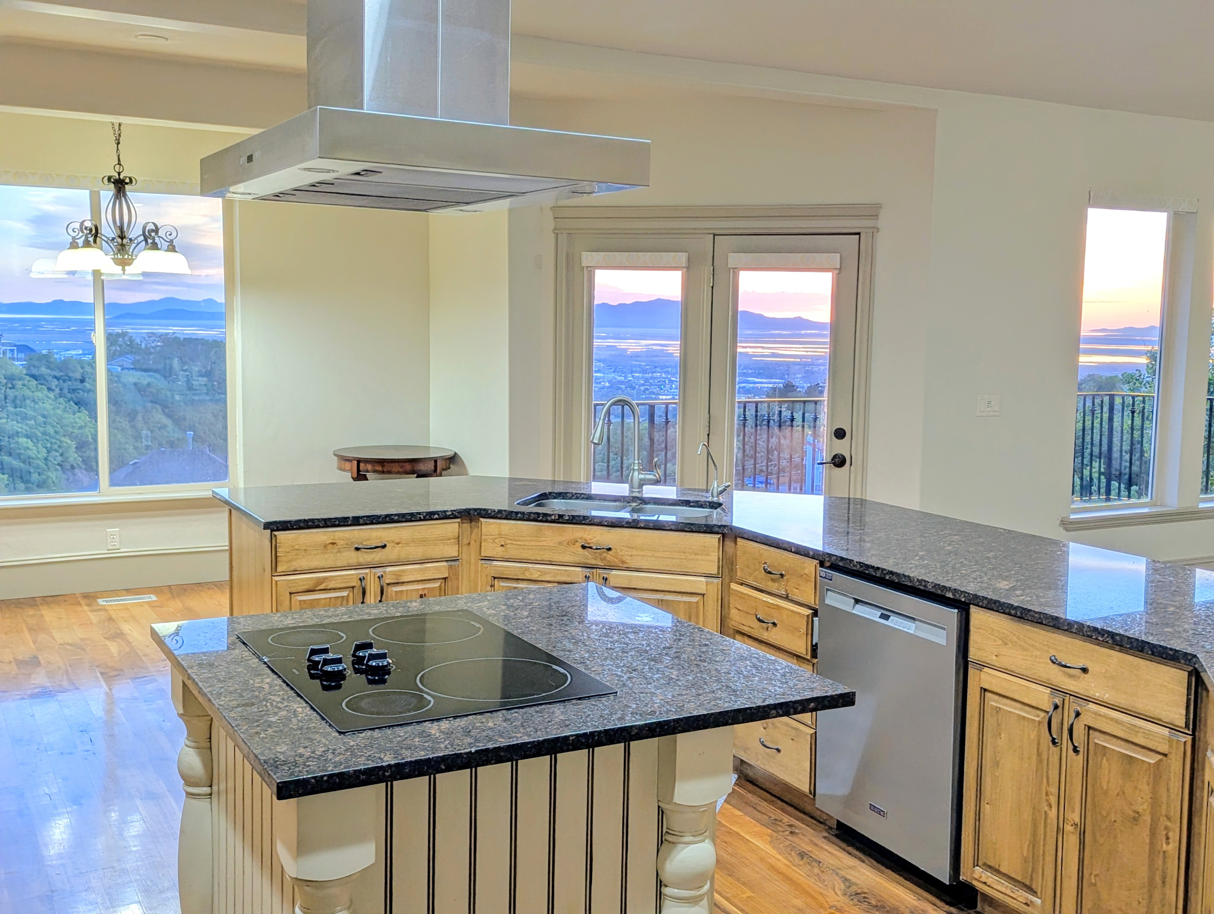 Kitchen with wood-finish flooring, dark stone countertops, wood cabinetry, and a large center island featuring a built-in cooktop