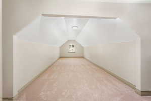 Expansive carpeted room featuring sloped ceilings, a window with muntins, and recessed lighting