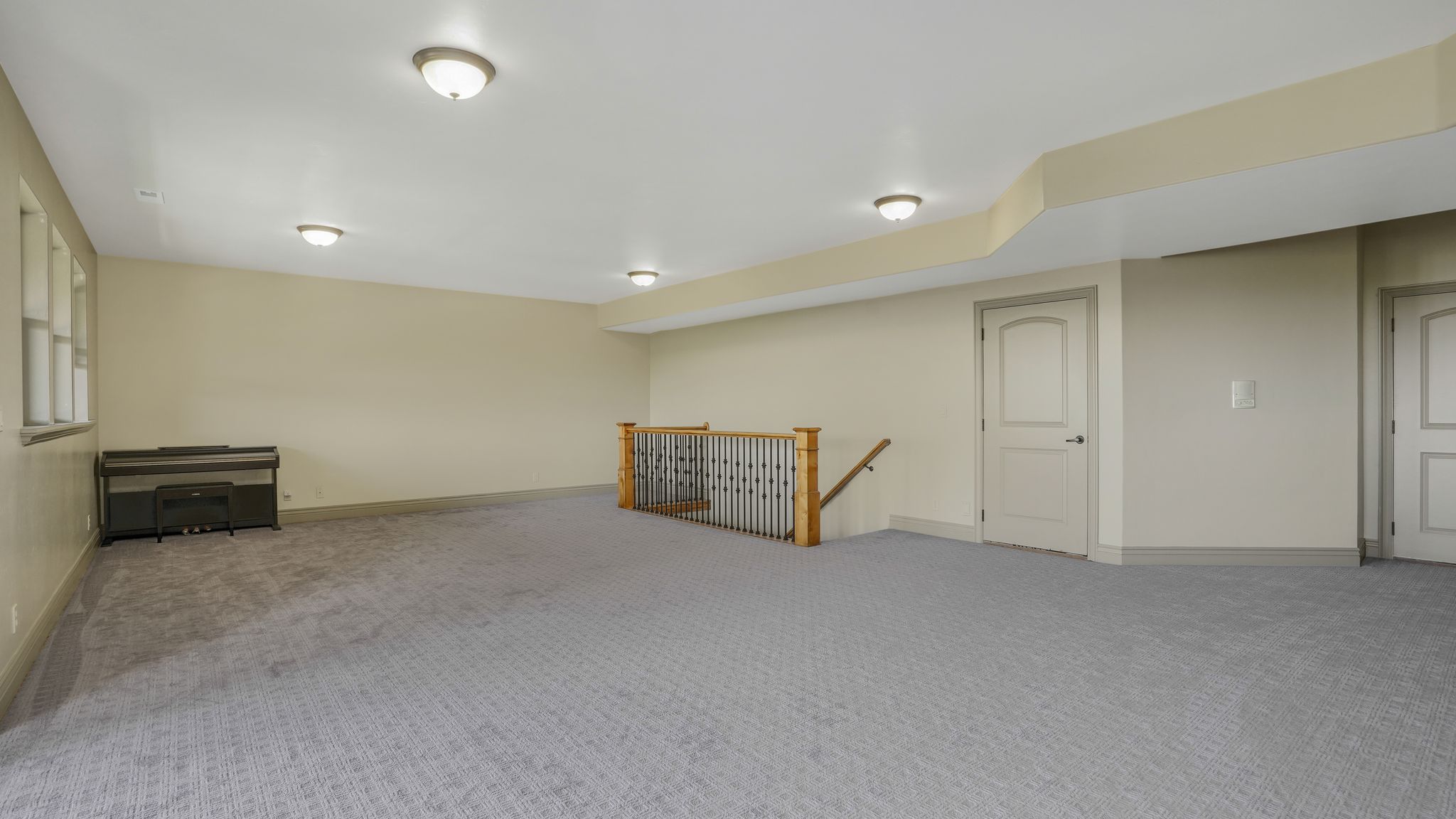 Spacious room featuring patterned gray carpeting, light beige walls, and multiple flush-mount ceiling lights