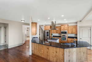 Kitchen featuring rich wood-finish flooring, light-toned cabinetry, stainless steel appliances, a range hood, and dark countertops
