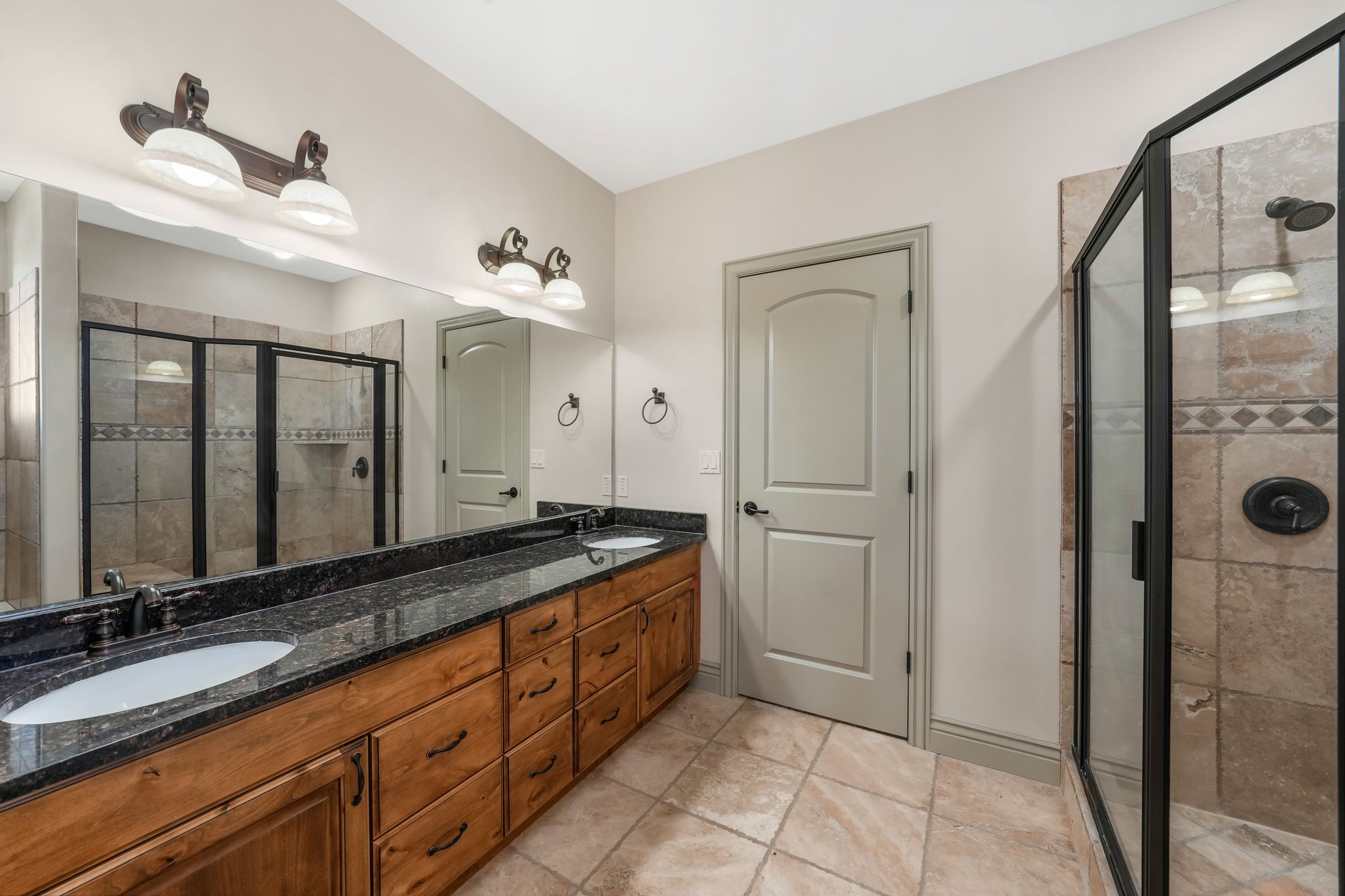 Dual vanity with a black stone countertop, integrated sinks, and bronze-finish fixtures