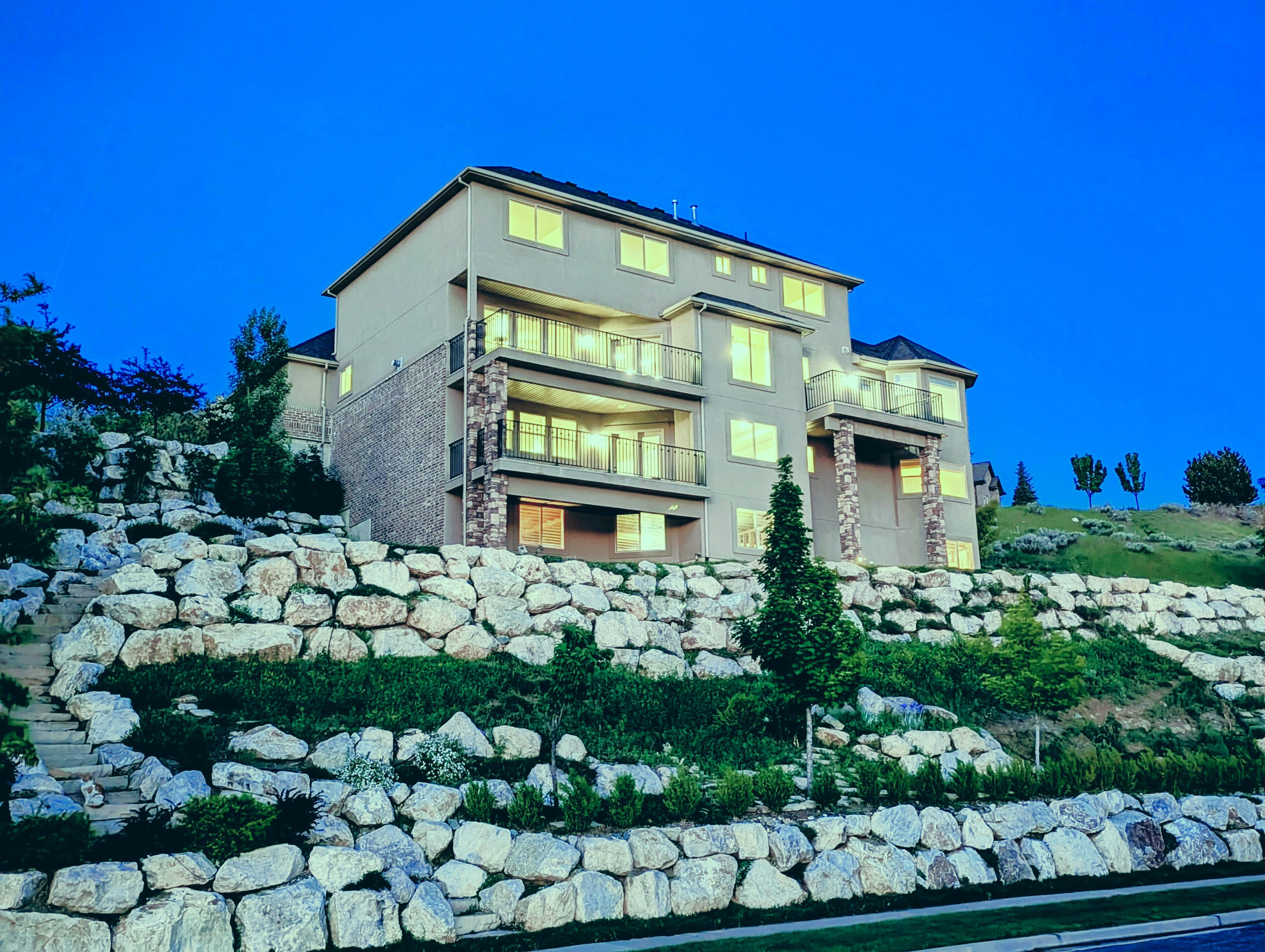 Multi-level residence featuring a stone-clad retaining wall, stone pillars, and multiple balconies with glass railings