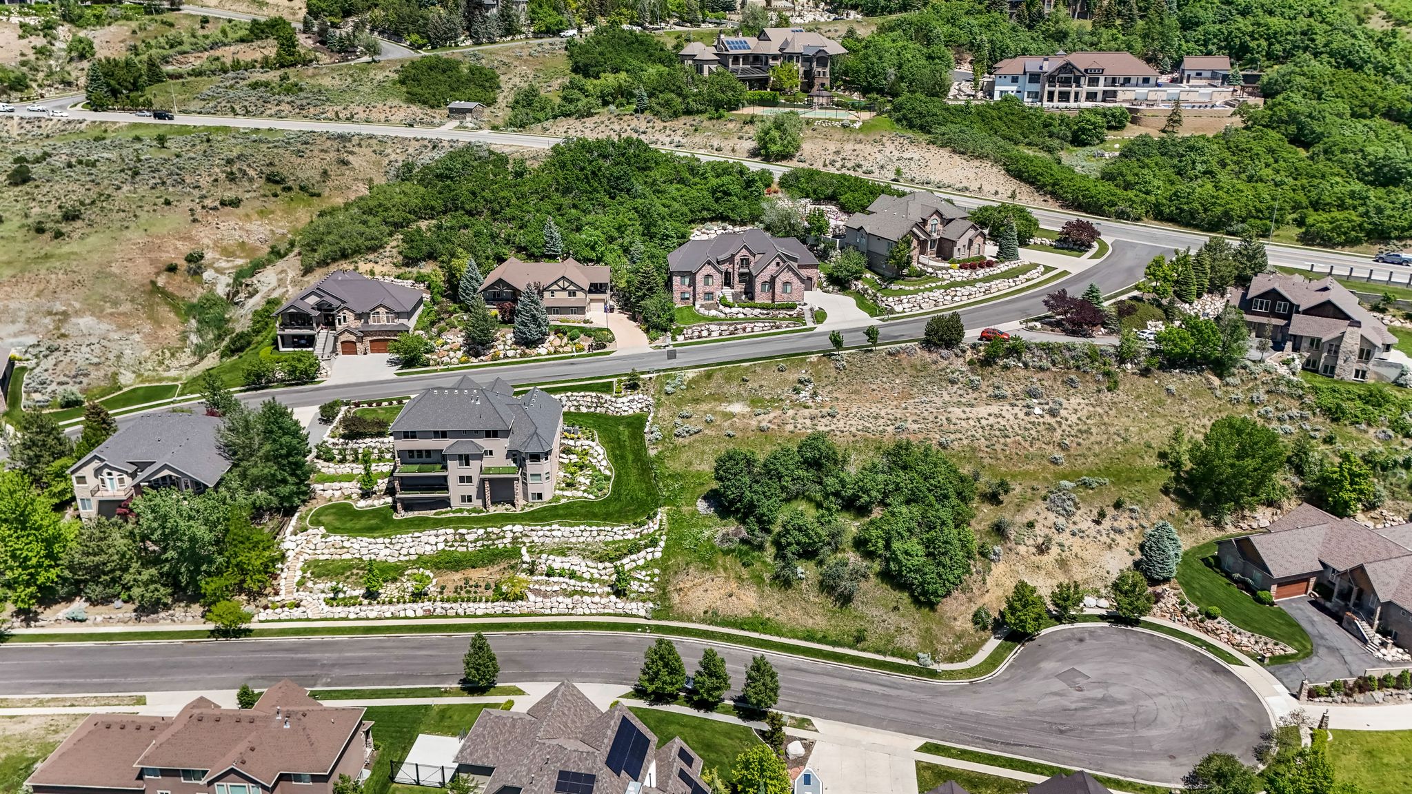 Hillside property featuring terraced landscaping with retaining walls, established tree coverage, and paved roads